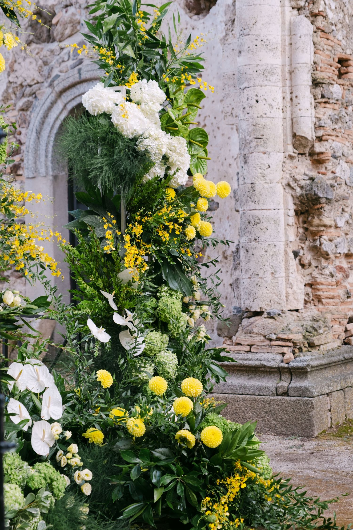 Yellow and white floral arrangements adorn stone archways in ancient ruins.