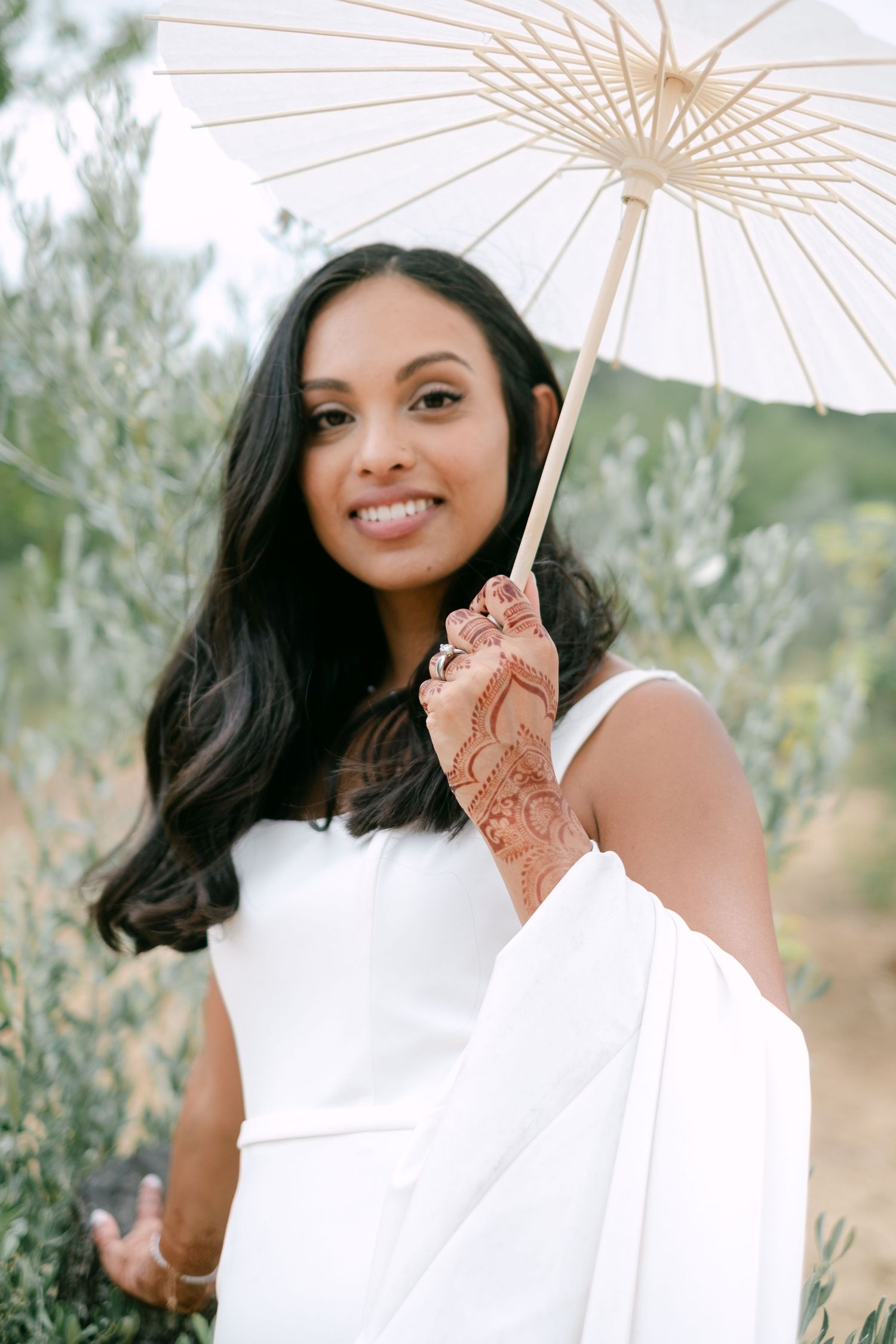 A person in a white dress holds a delicate paper parasol while posing outdoors against a natural backdrop.