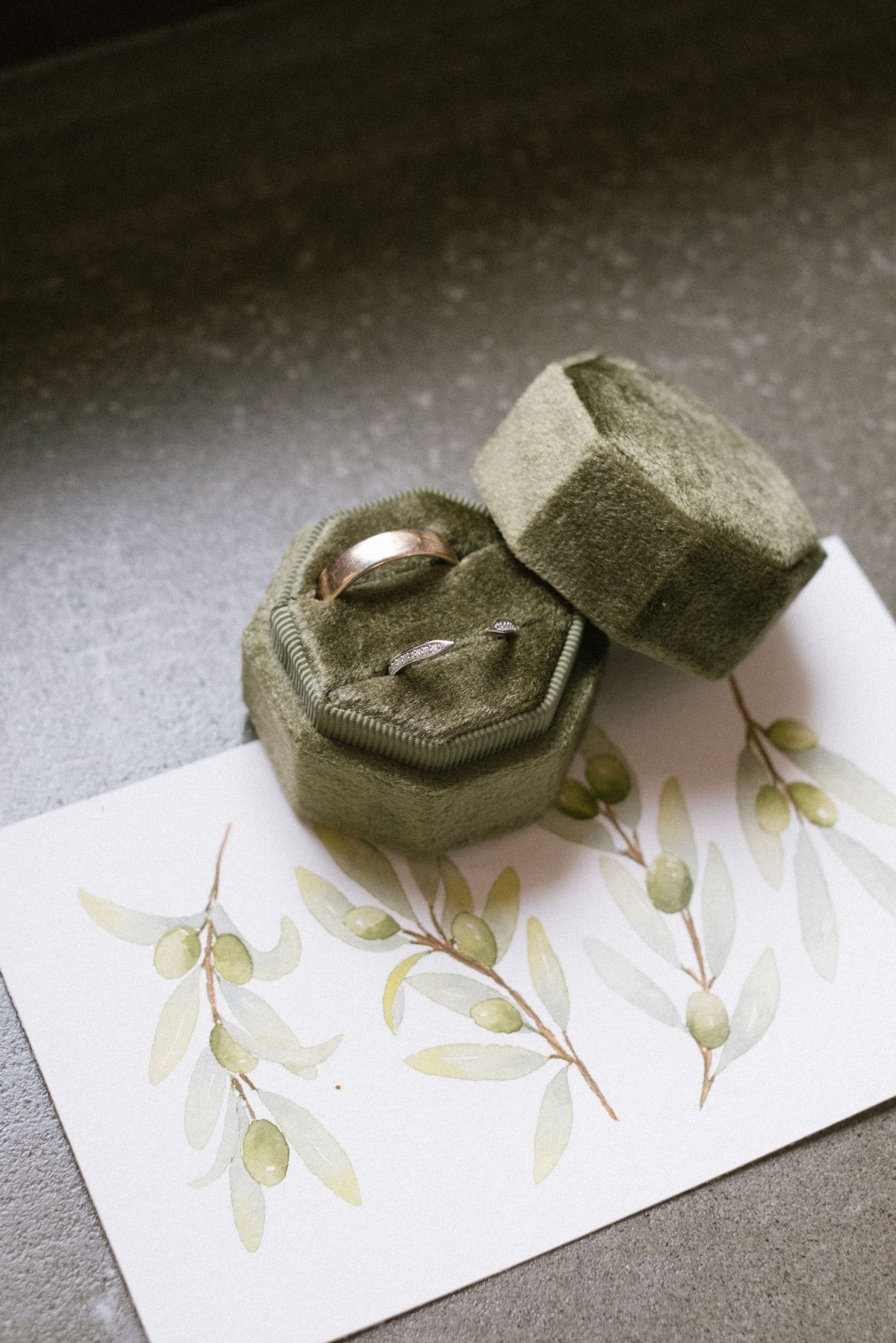 Wedding rings displayed in an olive green velvet ring box on a delicate floral watercolor card.