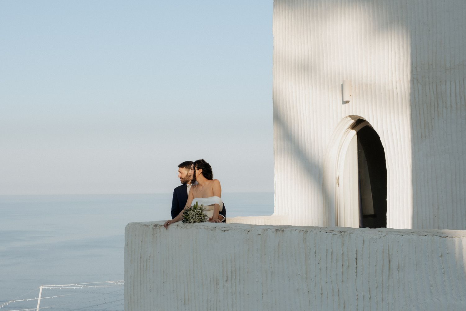 Minimalist white architecture frames a romantic coastal wedding scene.