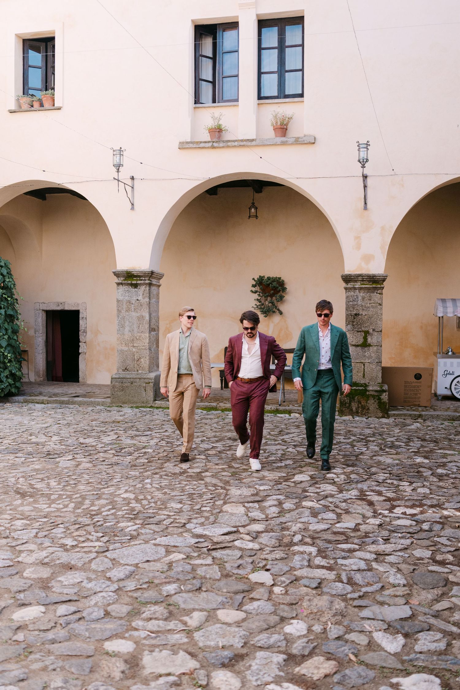 Three stylishly dressed figures walk through an elegant stone archway courtyard.