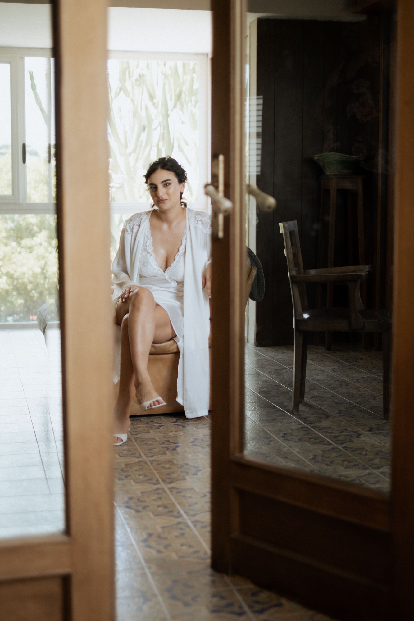 Through a glass door, a white robe and tiled floor are visible in a sunlit interior space.