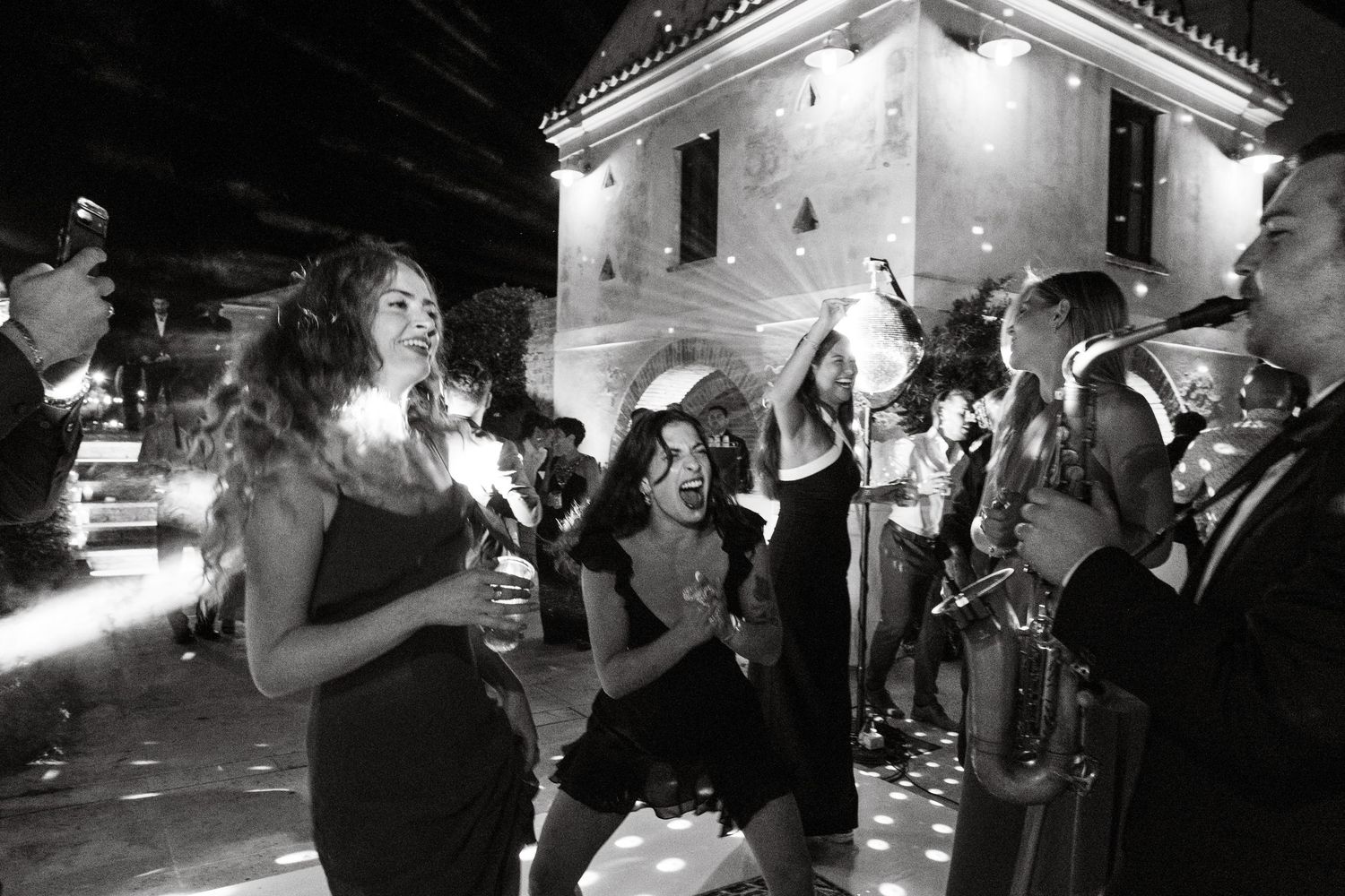 Wedding reception guests dancing and celebrating in dimly lit venue.