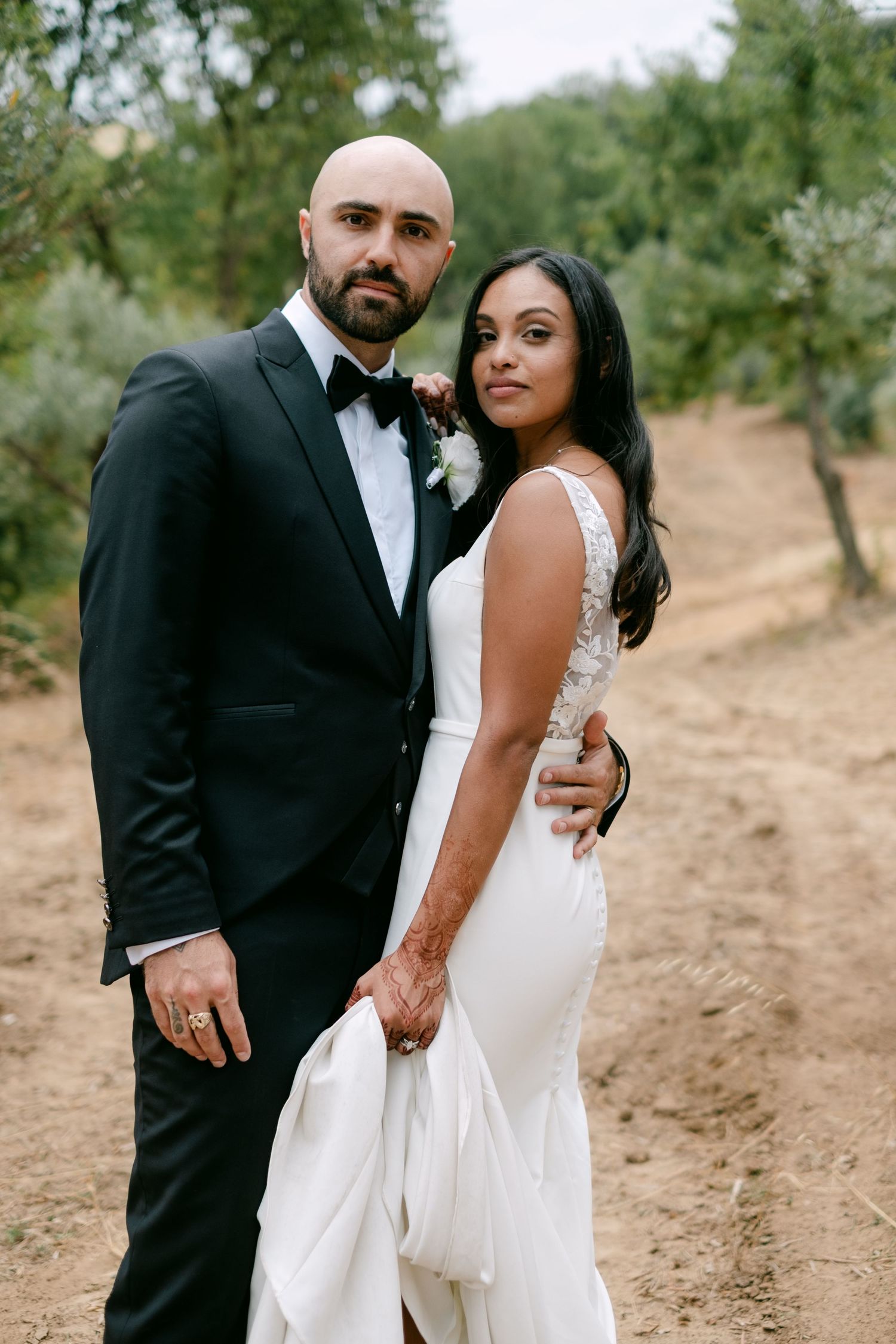 Couple in formal wedding attire posing together in an olive grove.