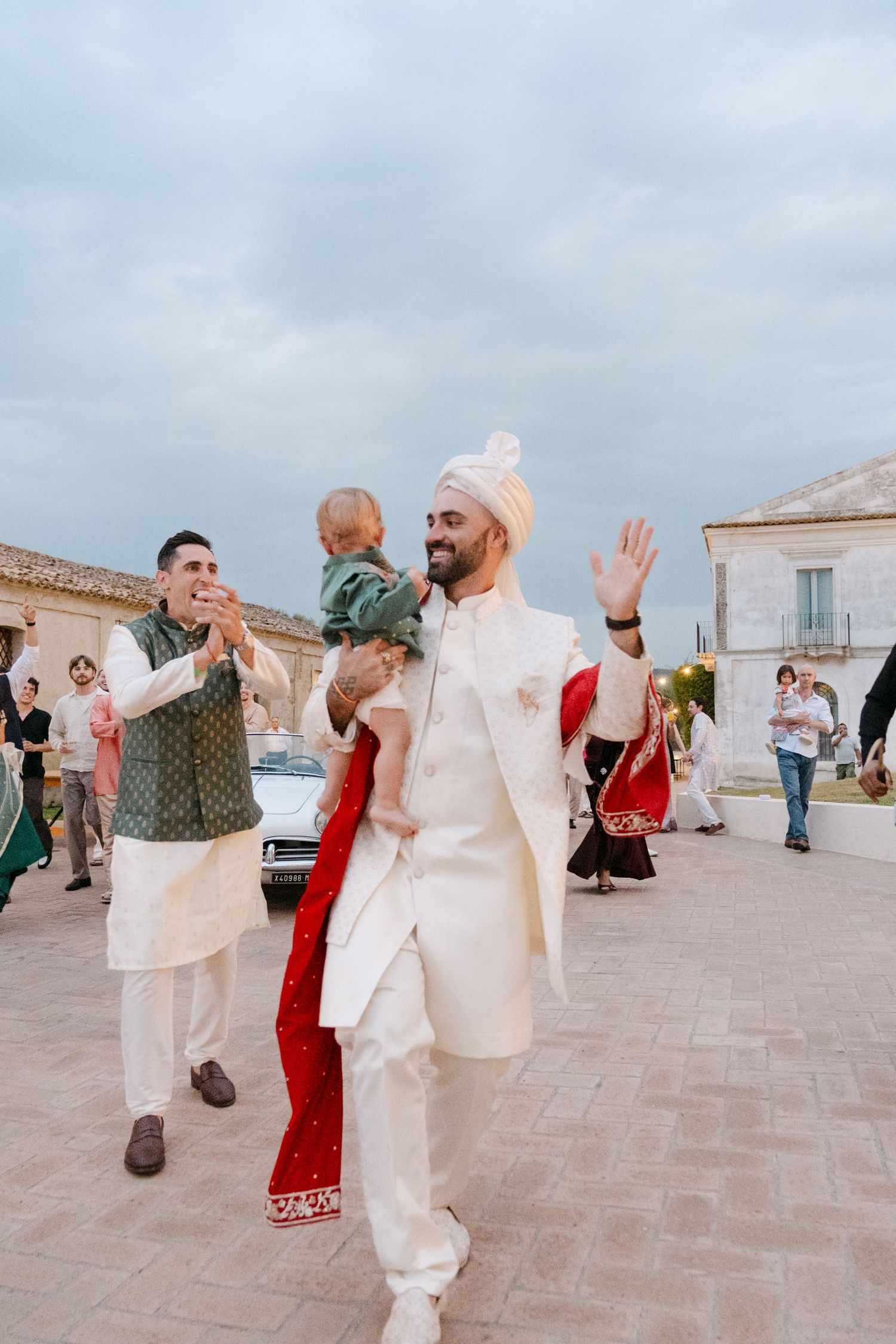 People in traditional white and red attire dance and celebrate on an outdoor terrace.