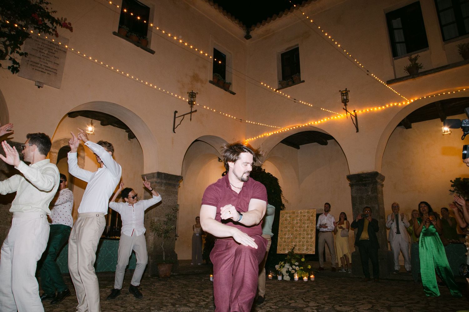 People dancing under string lights in an outdoor courtyard at night.