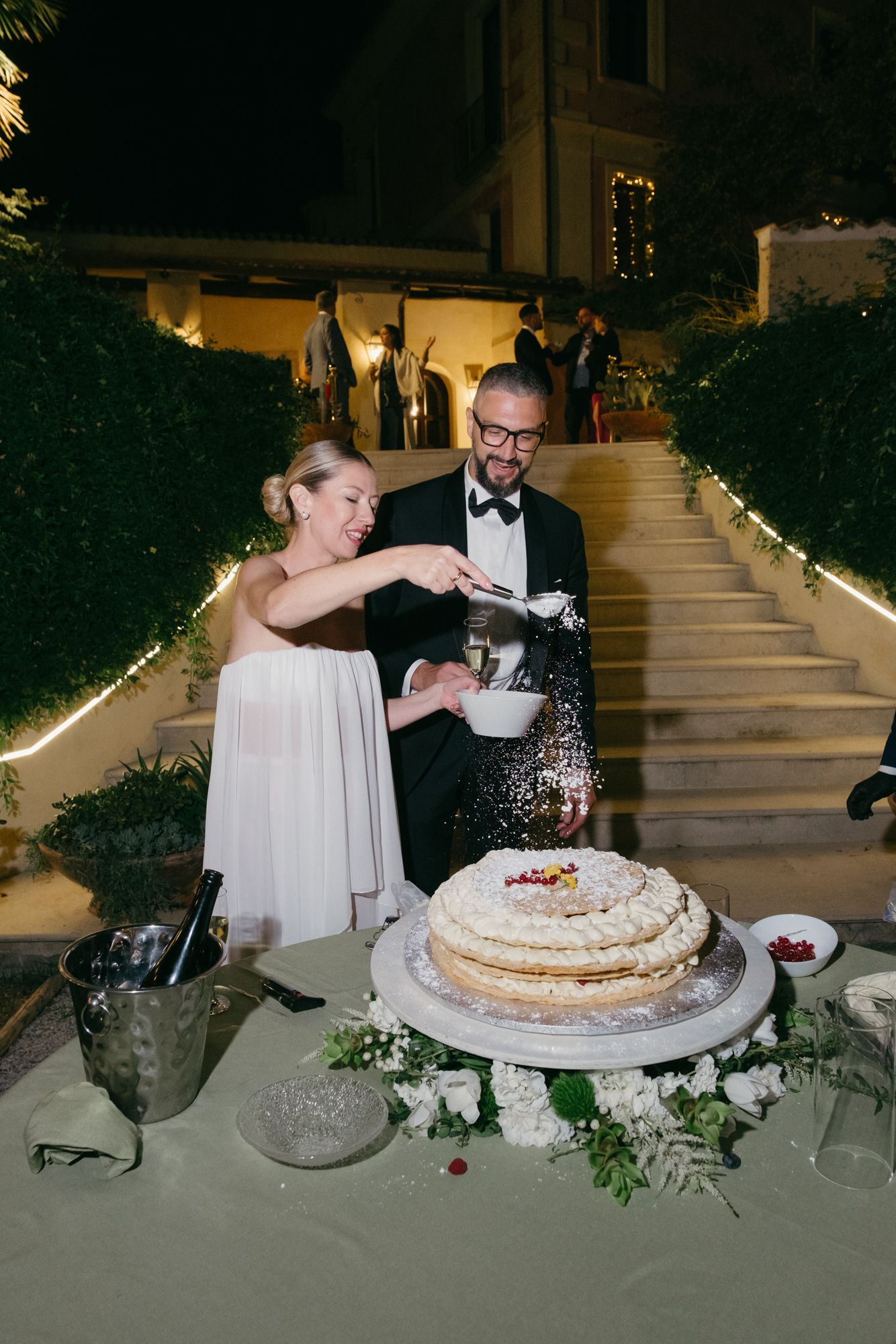 Couple sharing a playful moment while cutting their wedding cake at an evening reception.