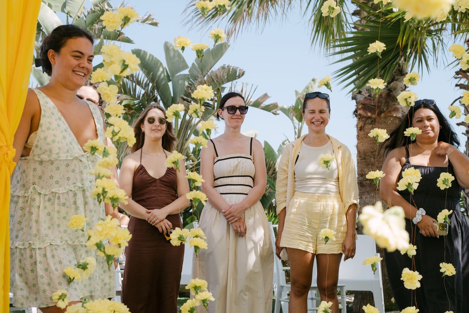 Wedding party celebrating outdoors with yellow and white floral decorations and palm trees.