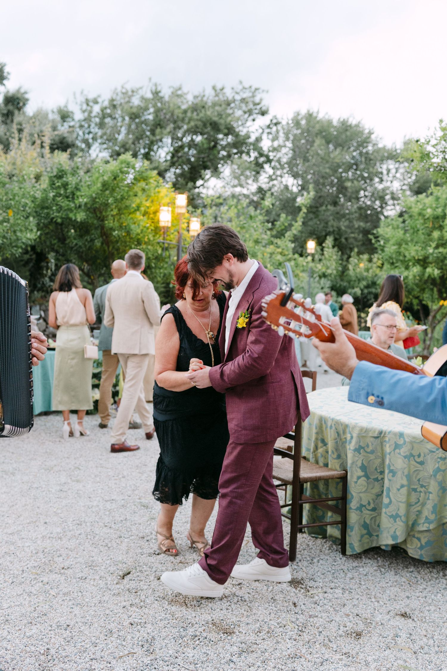 Wedding celebration on a gravel path with guests mingling around decorated tables outdoors.
