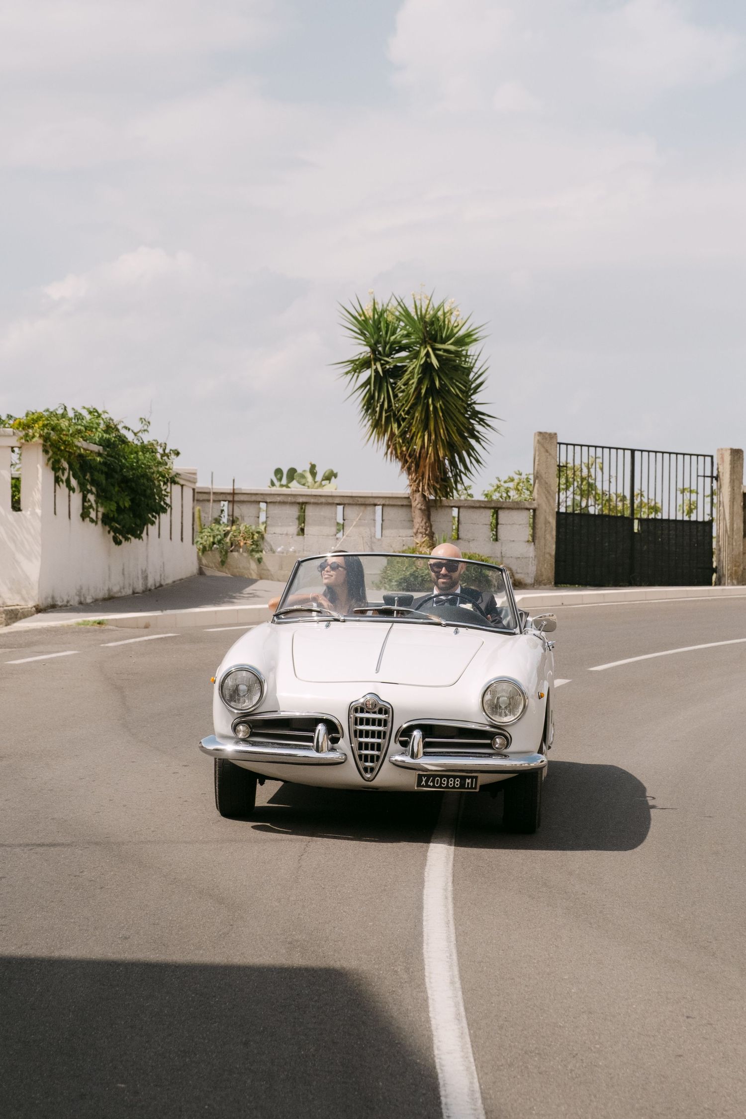 Classic silver Alfa Romeo sports car parked in a sunny rooftop lot with palm trees.