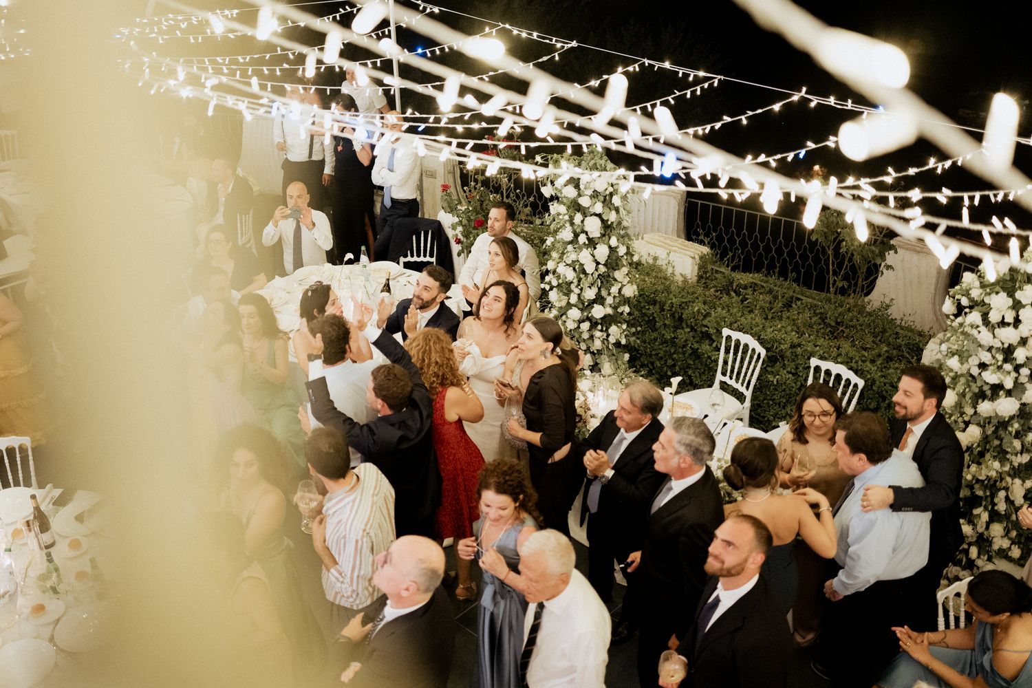 Wedding celebration under string lights with guests enjoying the festive atmosphere.