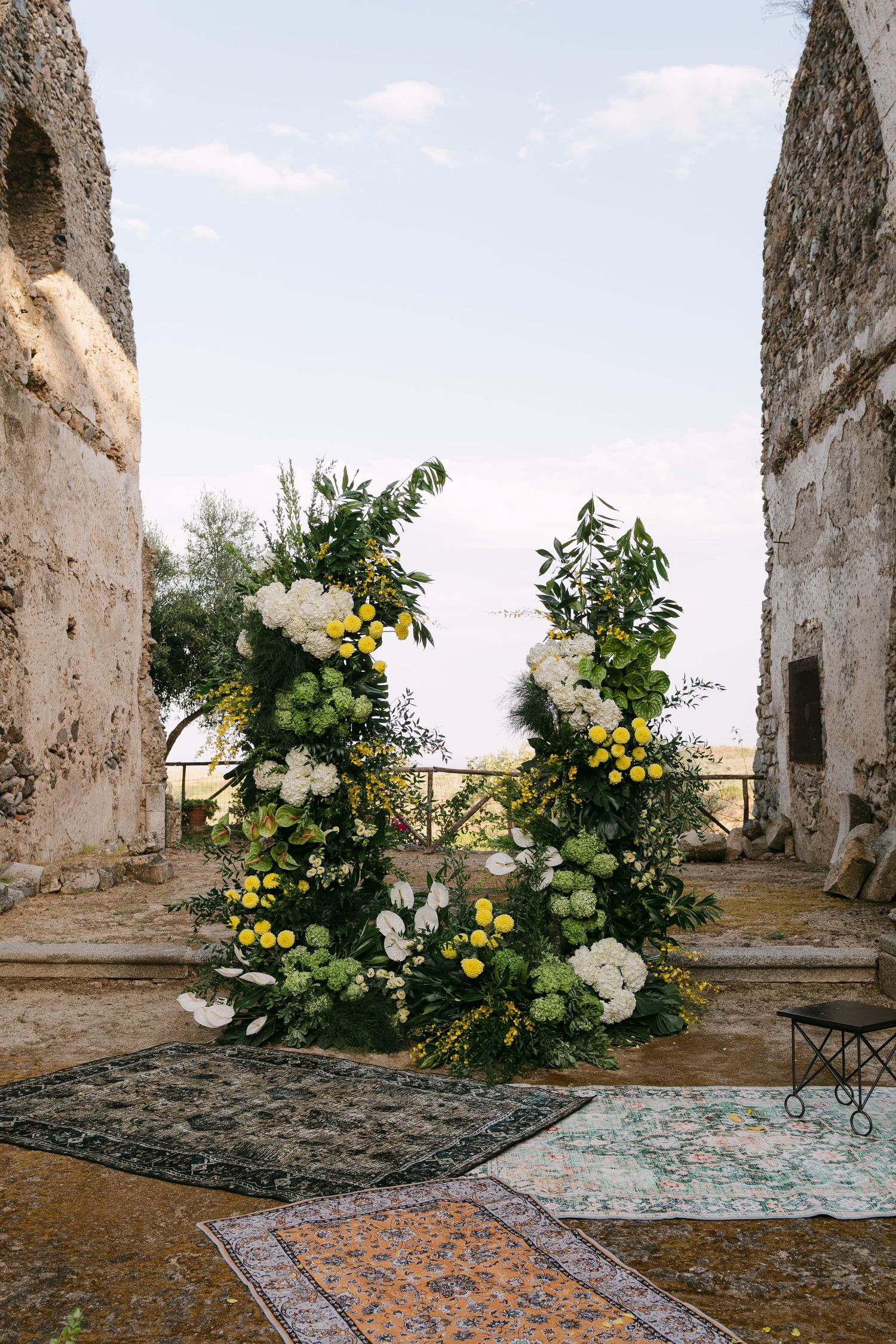 Beautiful floral arrangements with white and yellow blooms frame a rustic outdoor ceremony space.