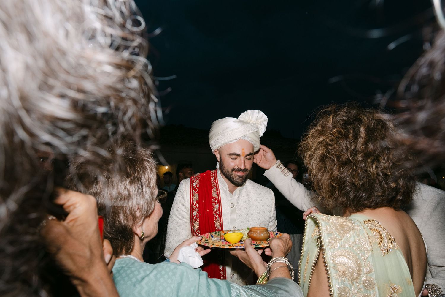 A person in traditional red vest serves food to guests during an evening celebration.