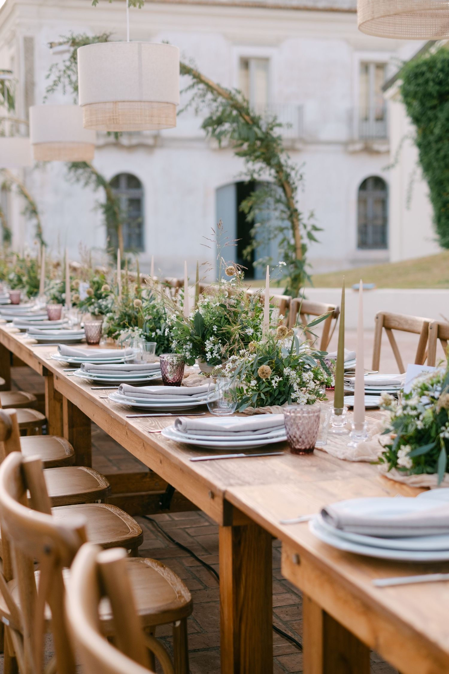 Elegant rustic wedding table setting with wooden chairs and fresh greenery decorations.