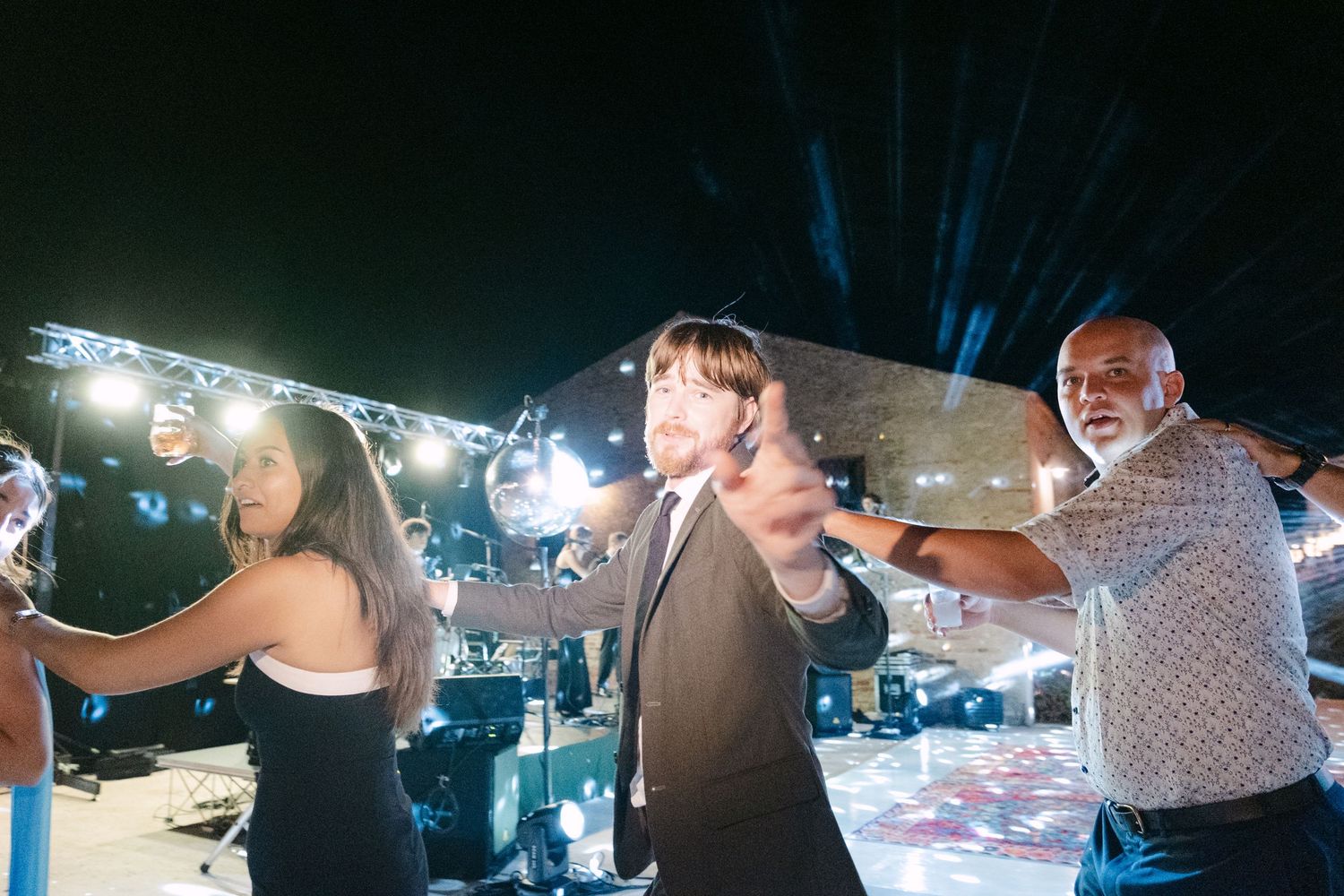 Evening wedding reception celebration with guests dancing under string lights.