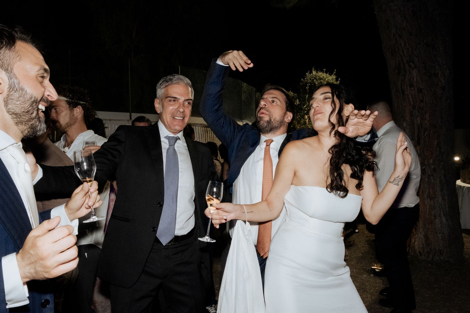 Wedding guests toasting and celebrating at a dimly lit outdoor reception.
