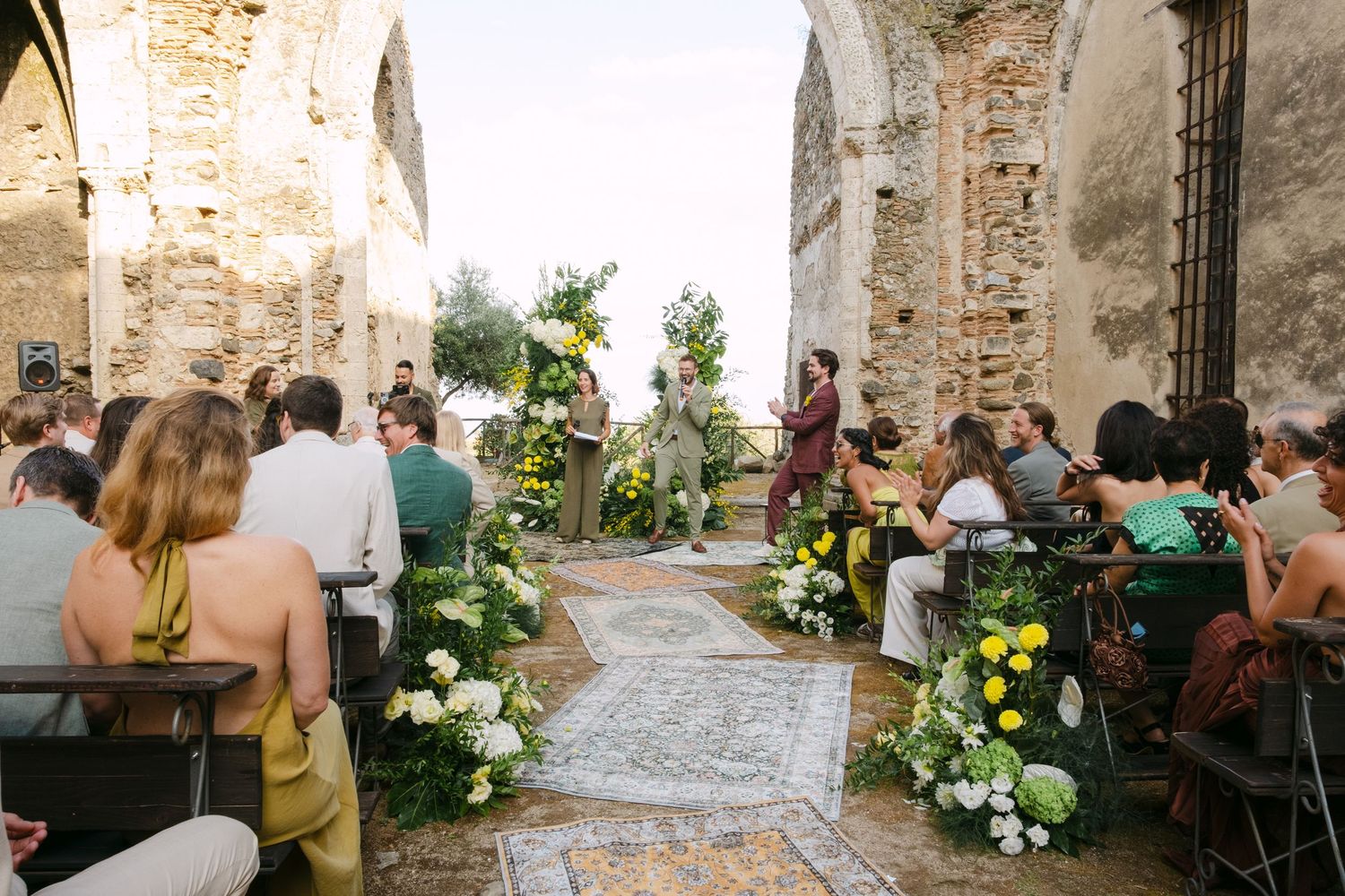 Wedding guests gather in a rustic stone courtyard with exposed brick walls and elegant floral arrangements.