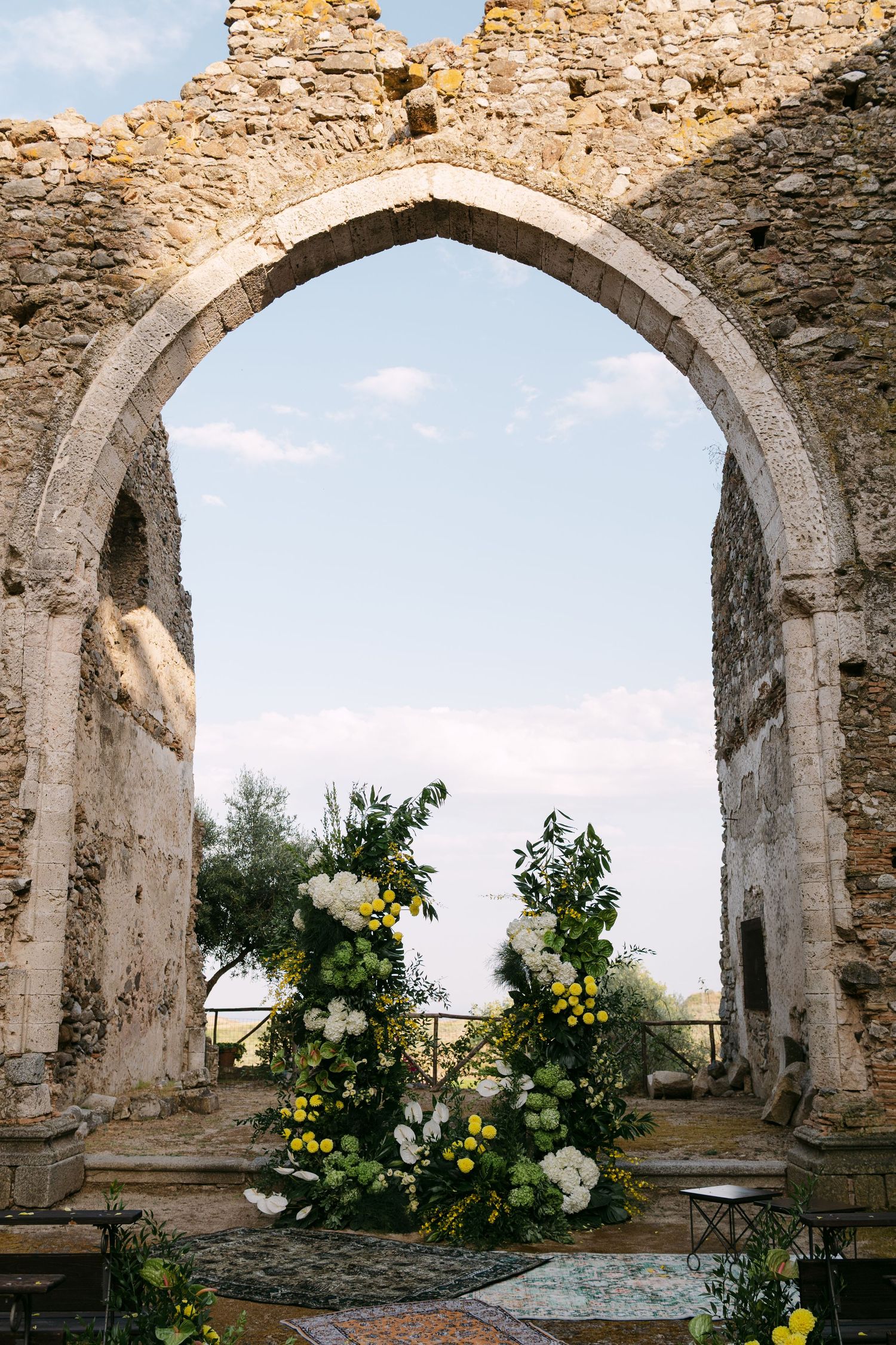 Stone archways decorated with white and yellow floral arrangements against blue sky.