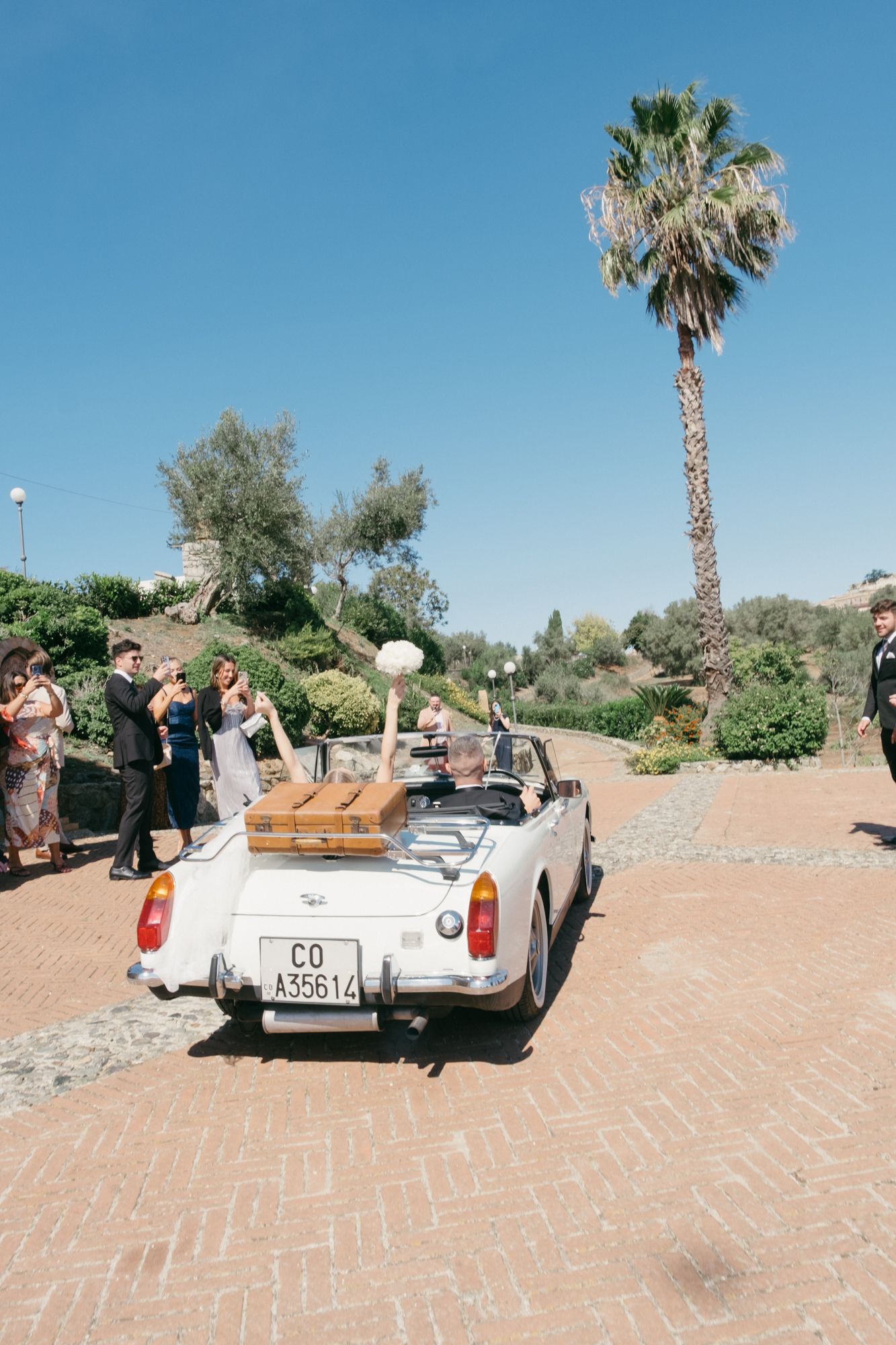 White vintage convertible car parked on brick pavement with palm trees in desert landscape.