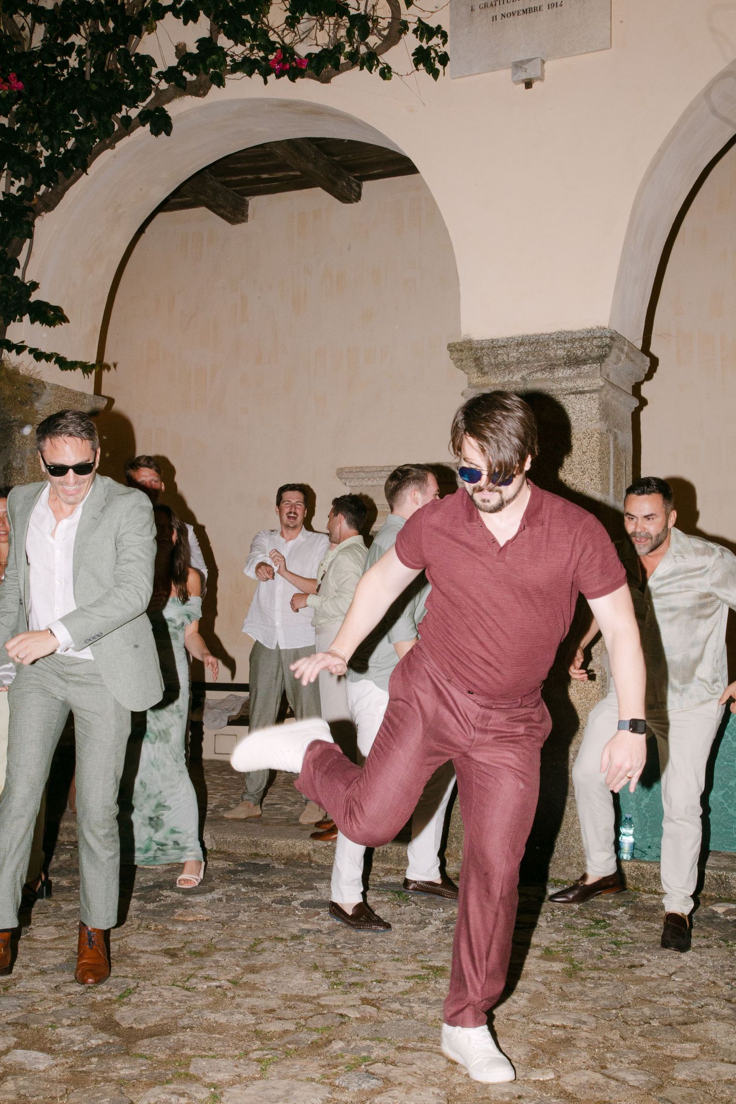 Energetic dance party with guests in casual attire under arched stone architecture.