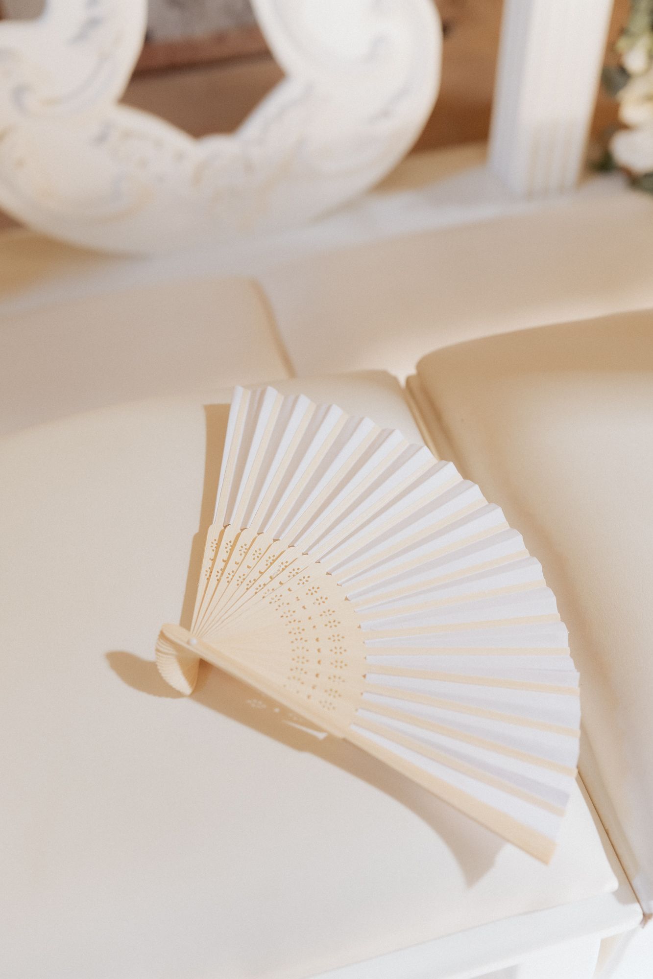 A white folding hand fan displayed on a light-colored surface.