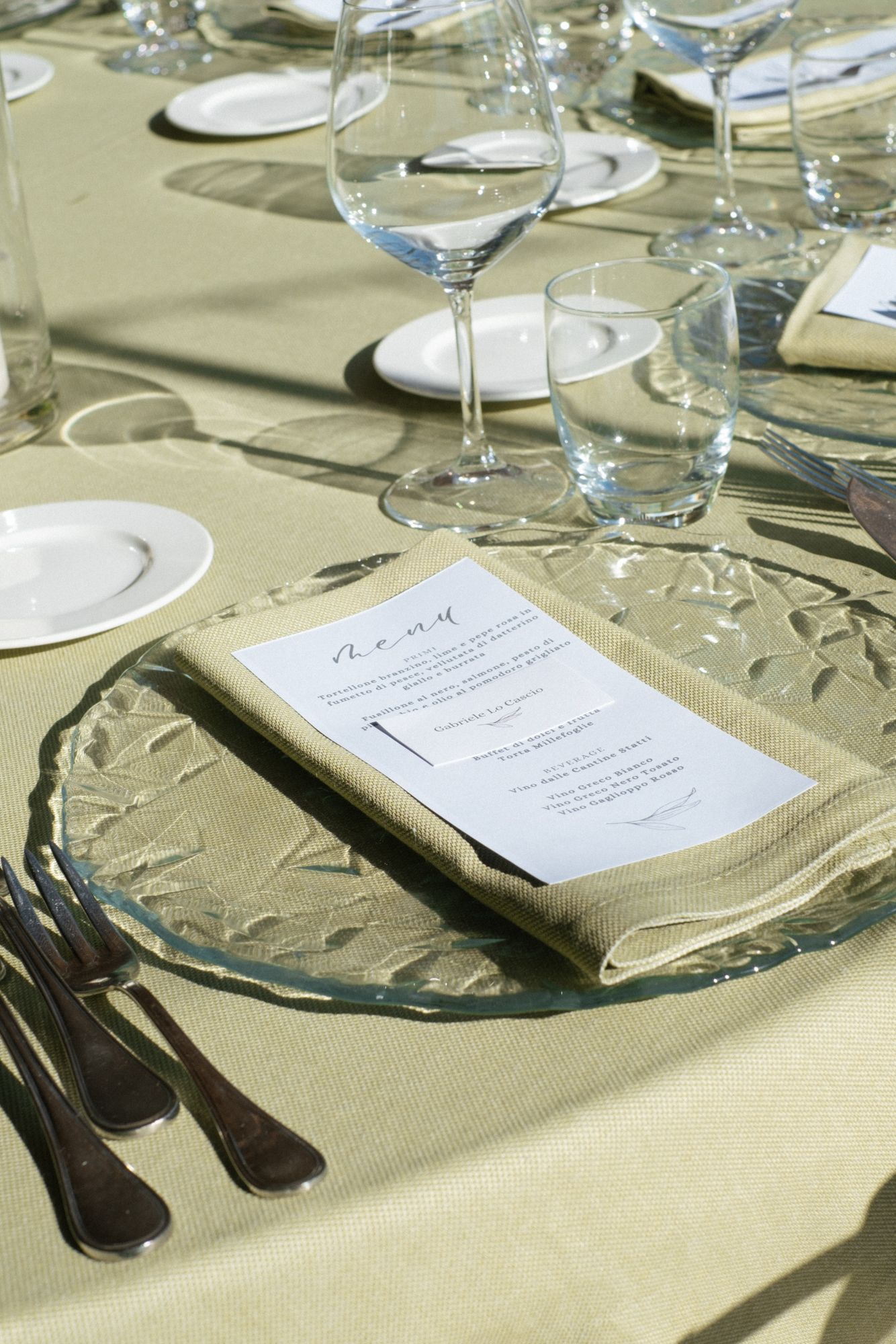 Elegant table settings with wine glasses and menus arranged on a beige tablecloth for a formal dining event.