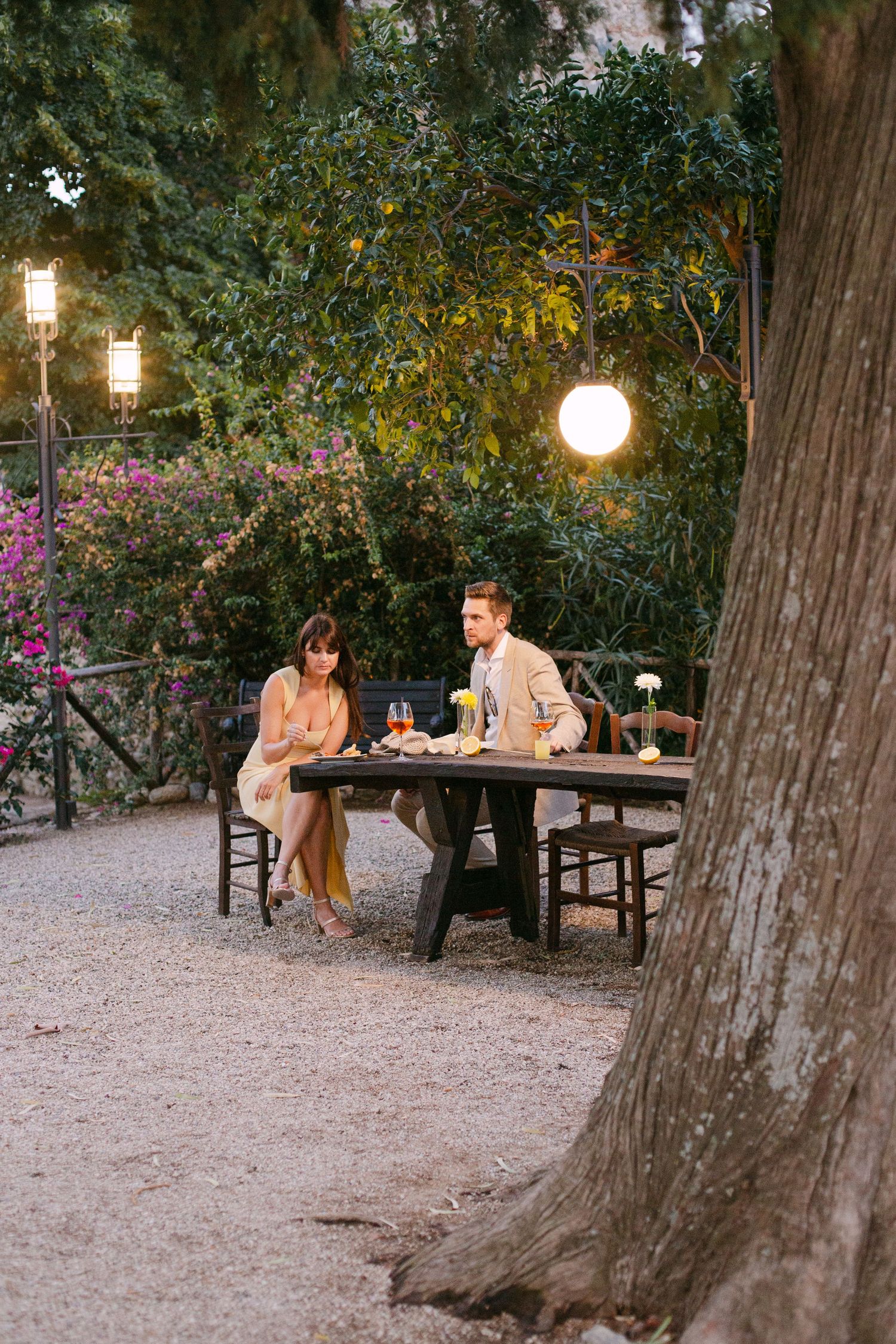 Outdoor evening reception with string lights hanging between large trees.