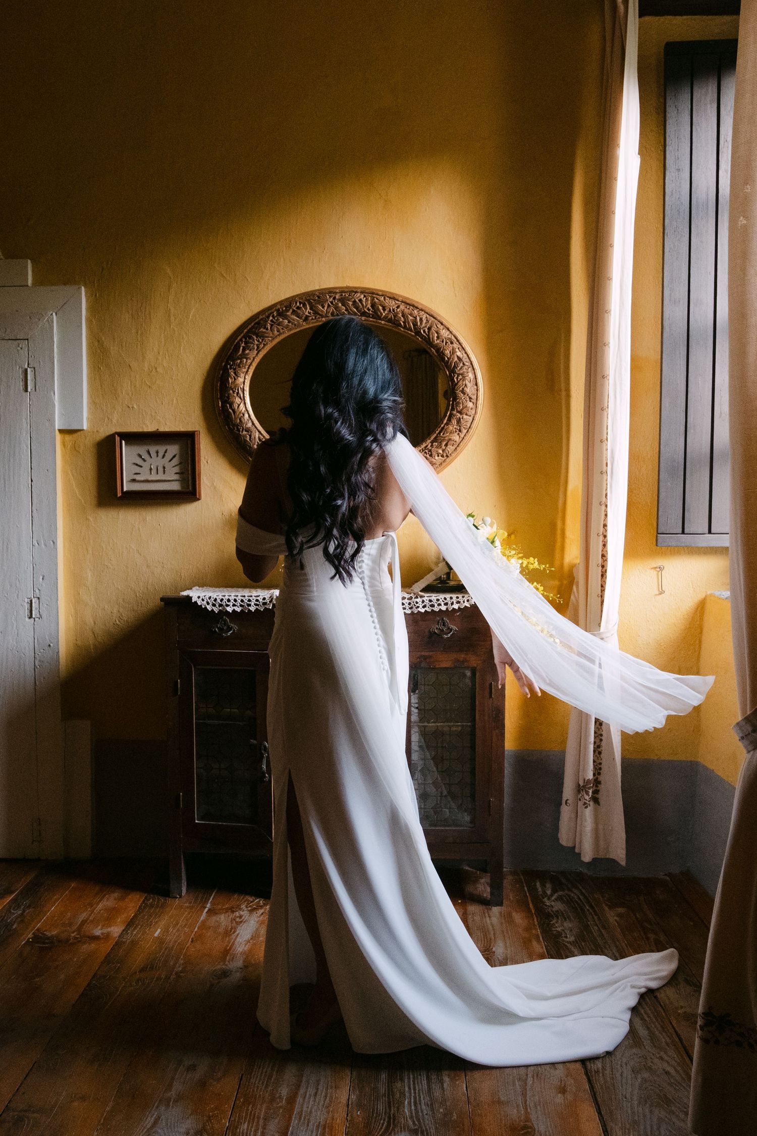 A flowing white wedding dress moves gracefully through a warmly lit vintage room with wooden floors.