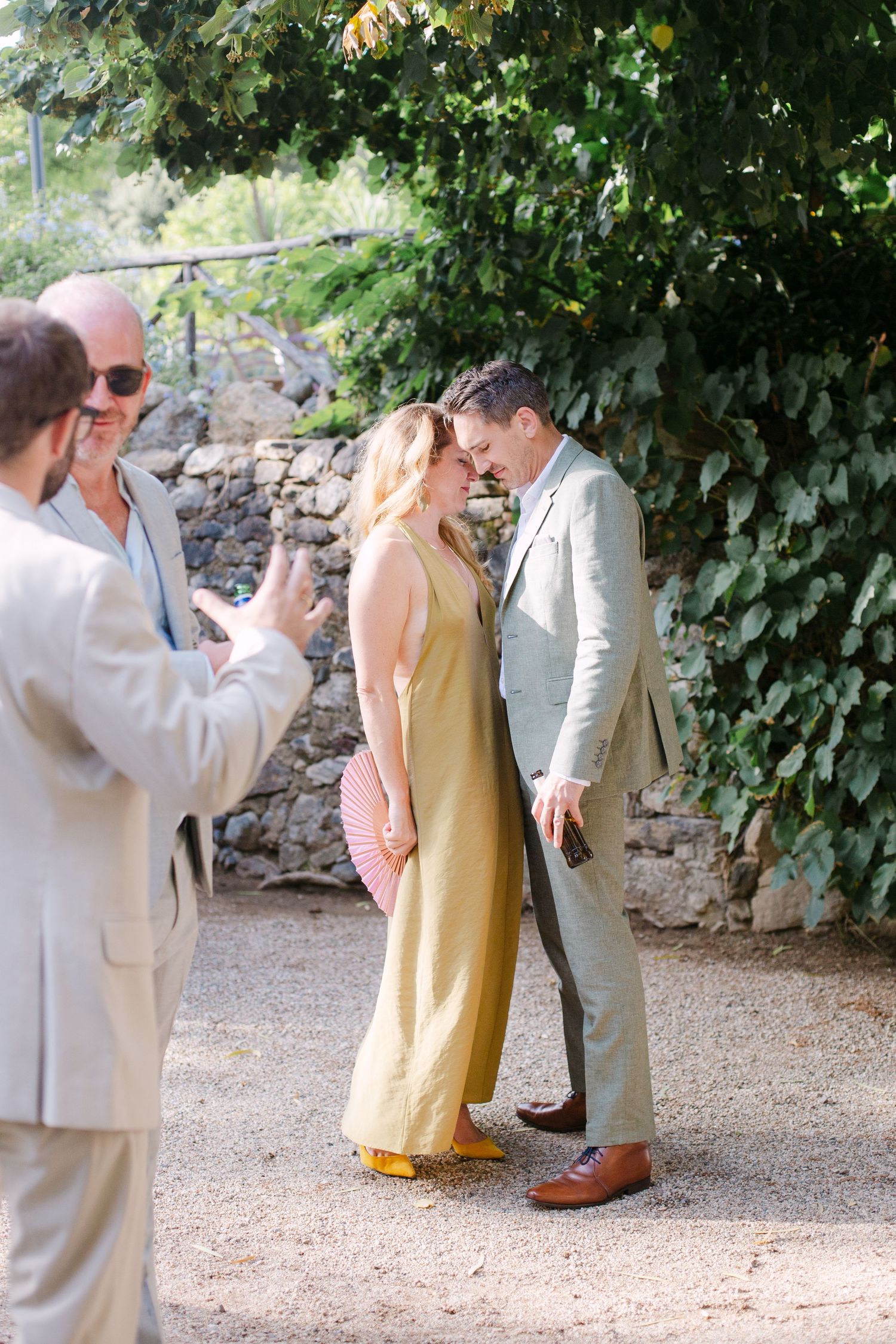 Wedding guests gather in a garden courtyard with stone walls and lush greenery.