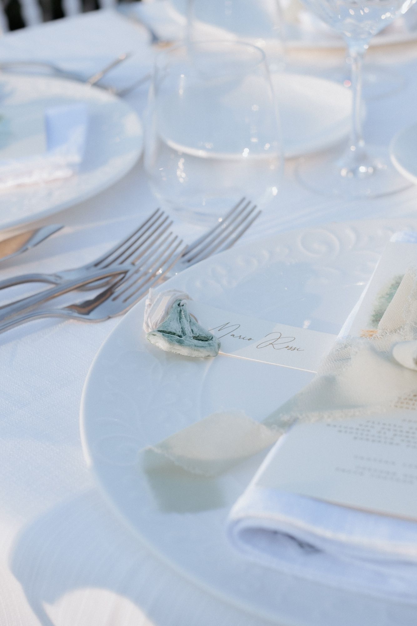 Elegant white table setting with silverware and place cards for a formal wedding reception.