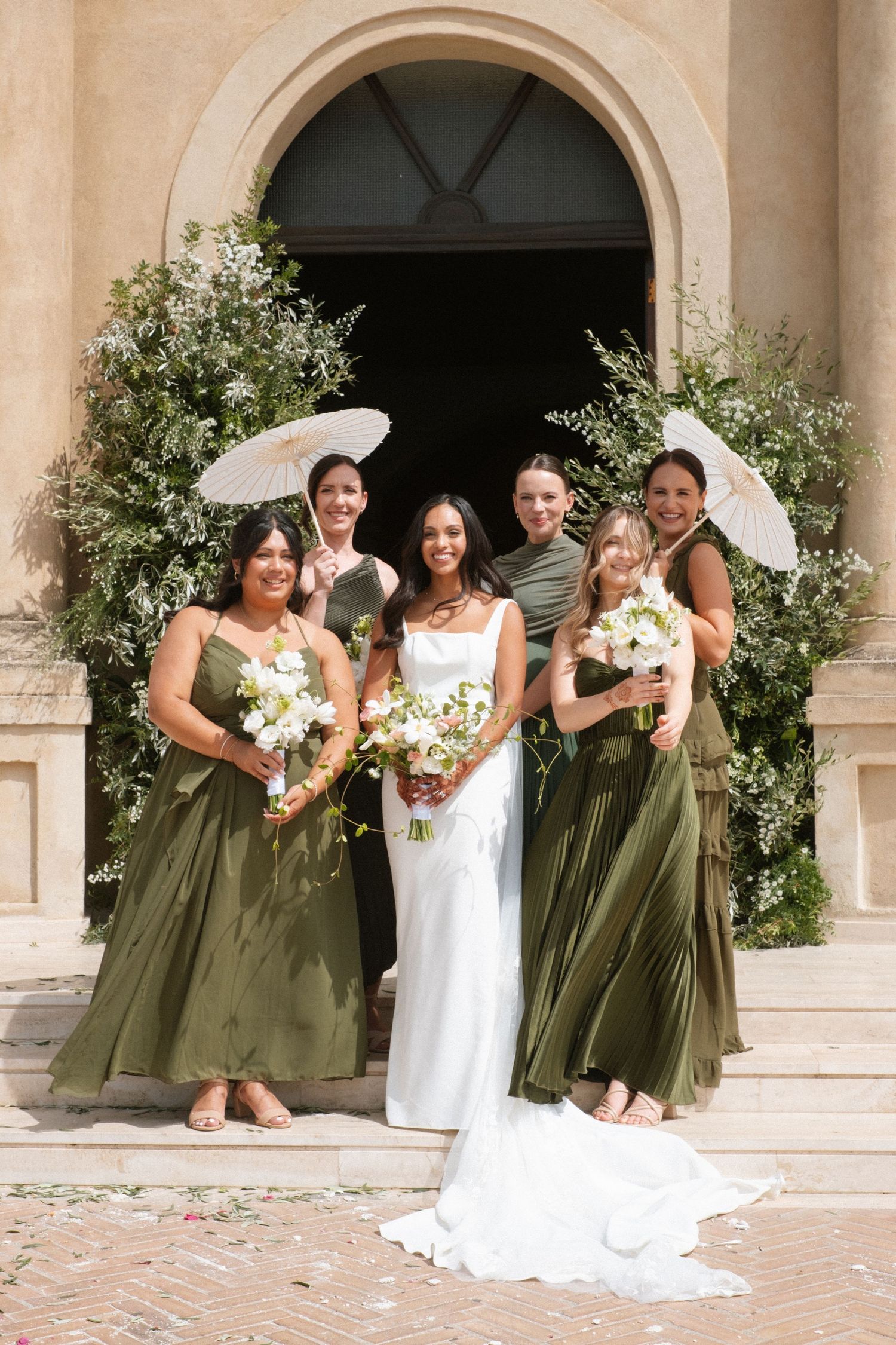 Wedding party poses on church steps with bridesmaids in olive green dresses.