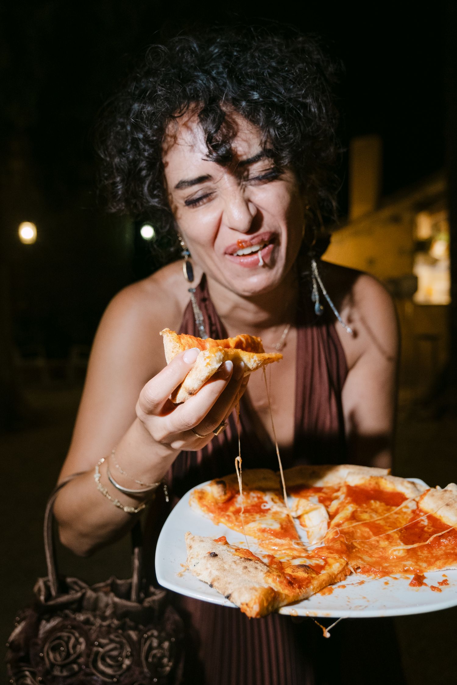 Person enjoying stretchy cheese pizza in dramatic nighttime lighting.