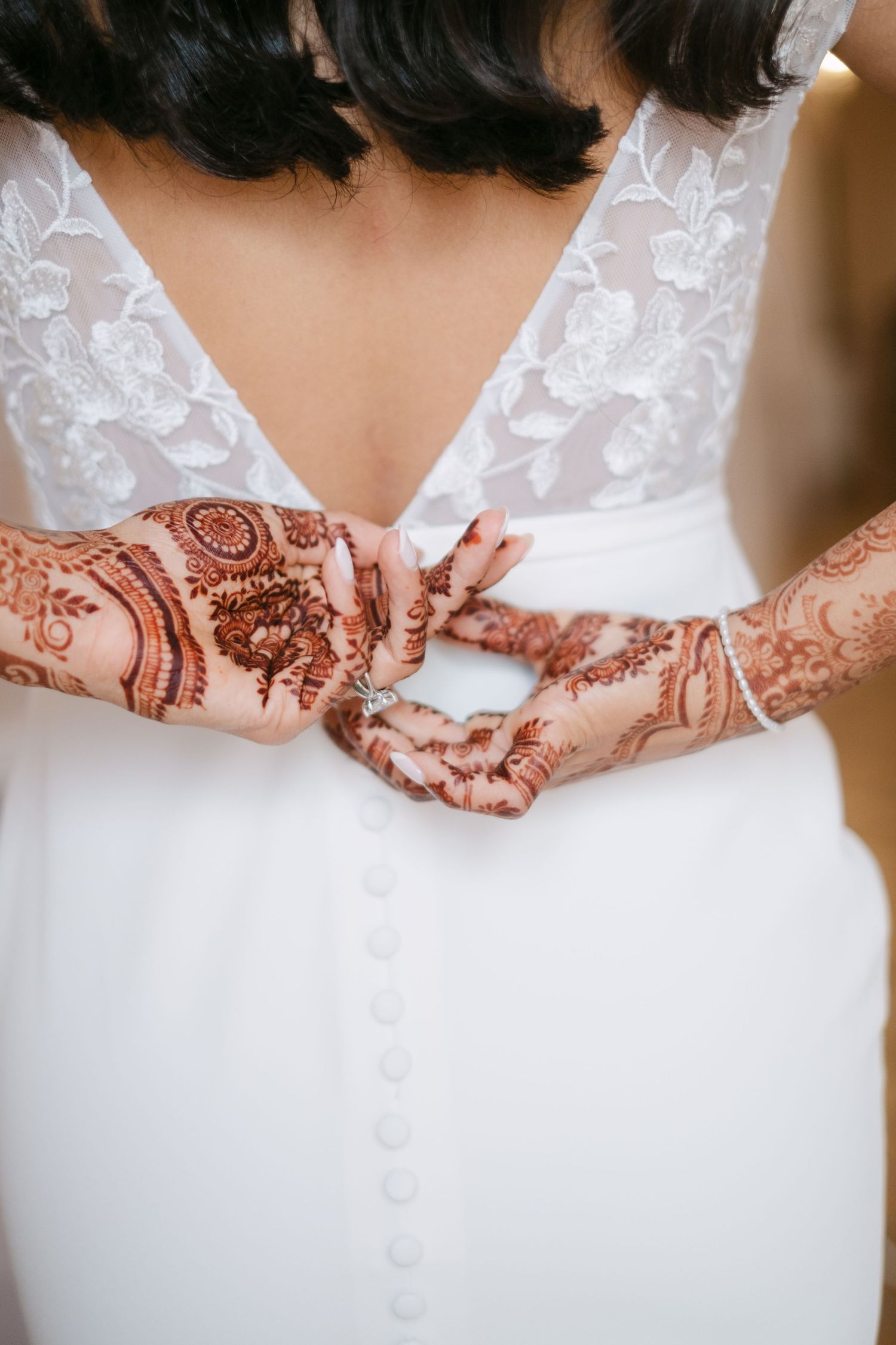 Close-up of intricate henna designs on hands against a white wedding dress background.
