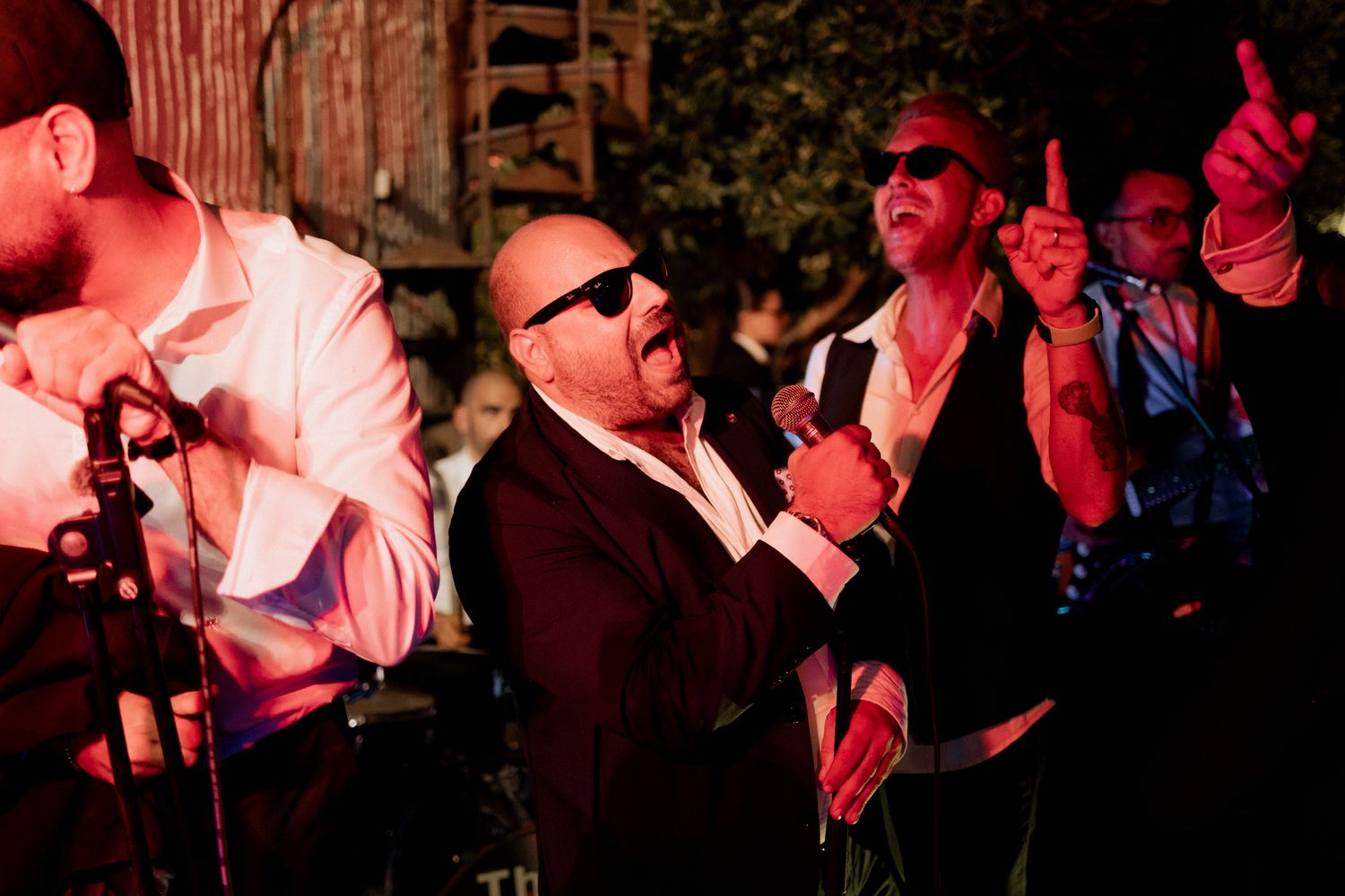 Wedding band performers in suits and sunglasses entertaining guests with energetic music.