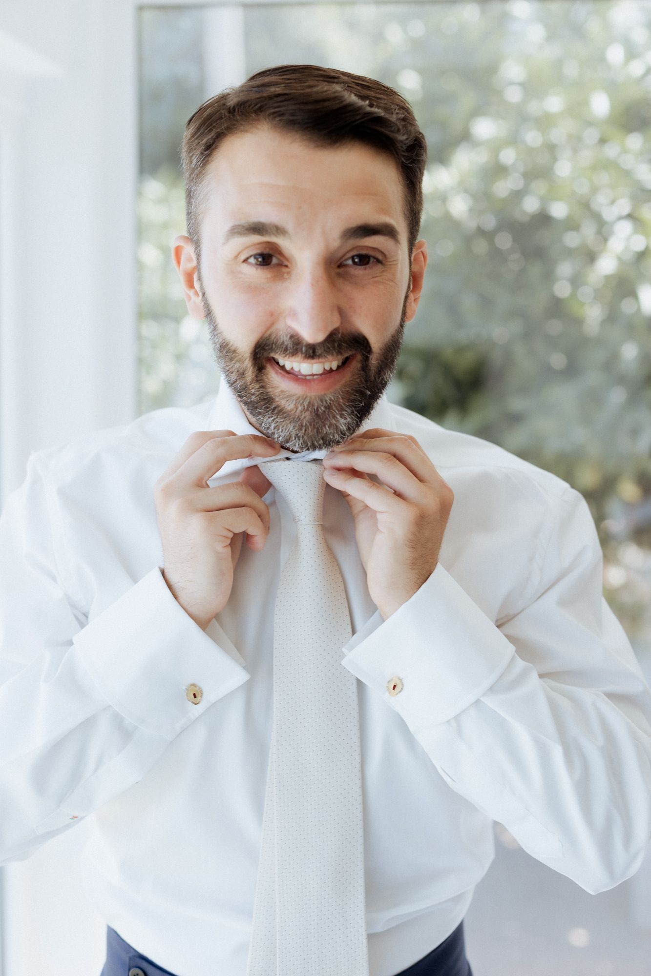 Person in white dress shirt adjusting their collar against a bright window background.