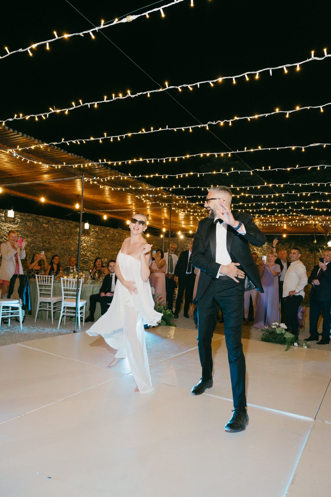 A wedding reception dance floor illuminated by romantic string lights hanging overhead at an indoor venue.
