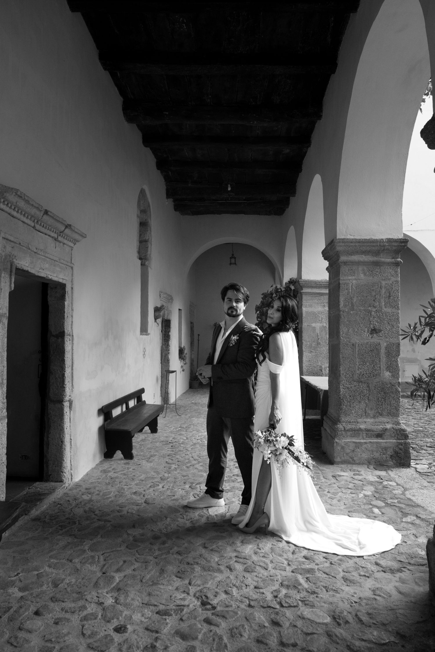 Black and white photos capture romantic moments between newlyweds in a historic stone corridor.