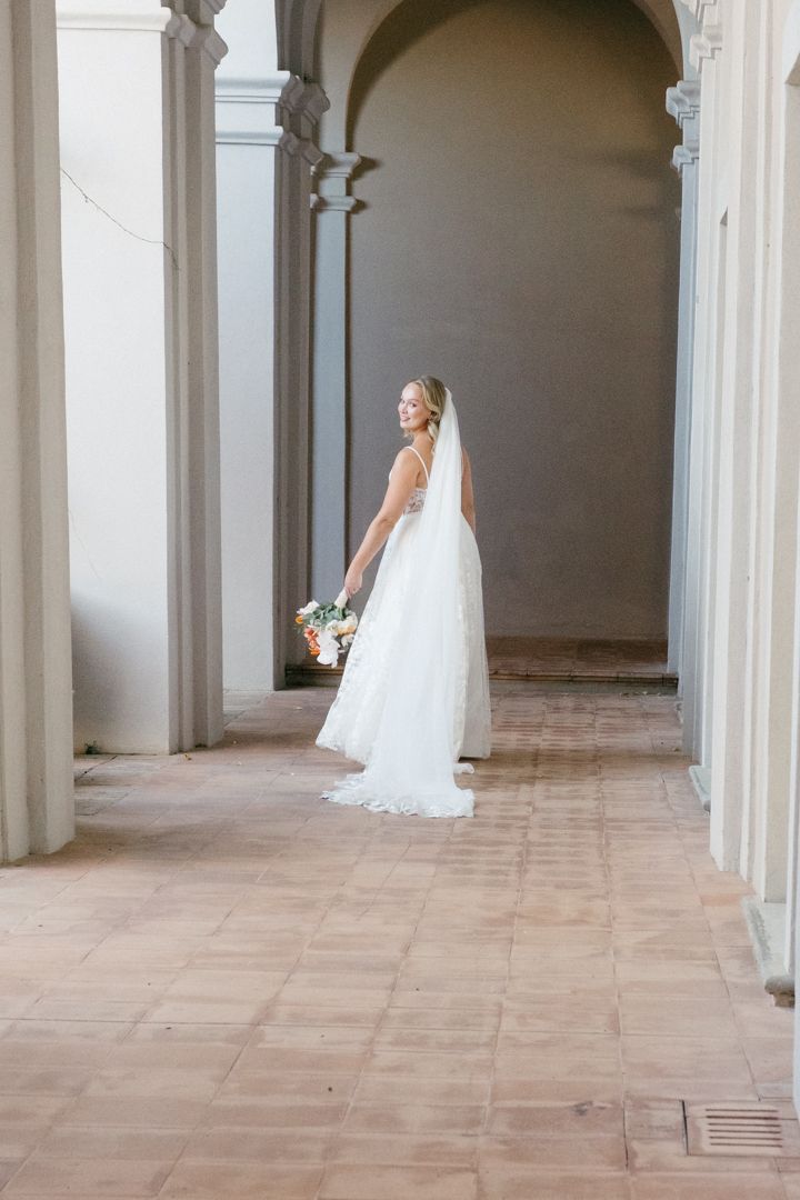 A classical arched corridor with stone columns and terra cotta flooring in natural light.