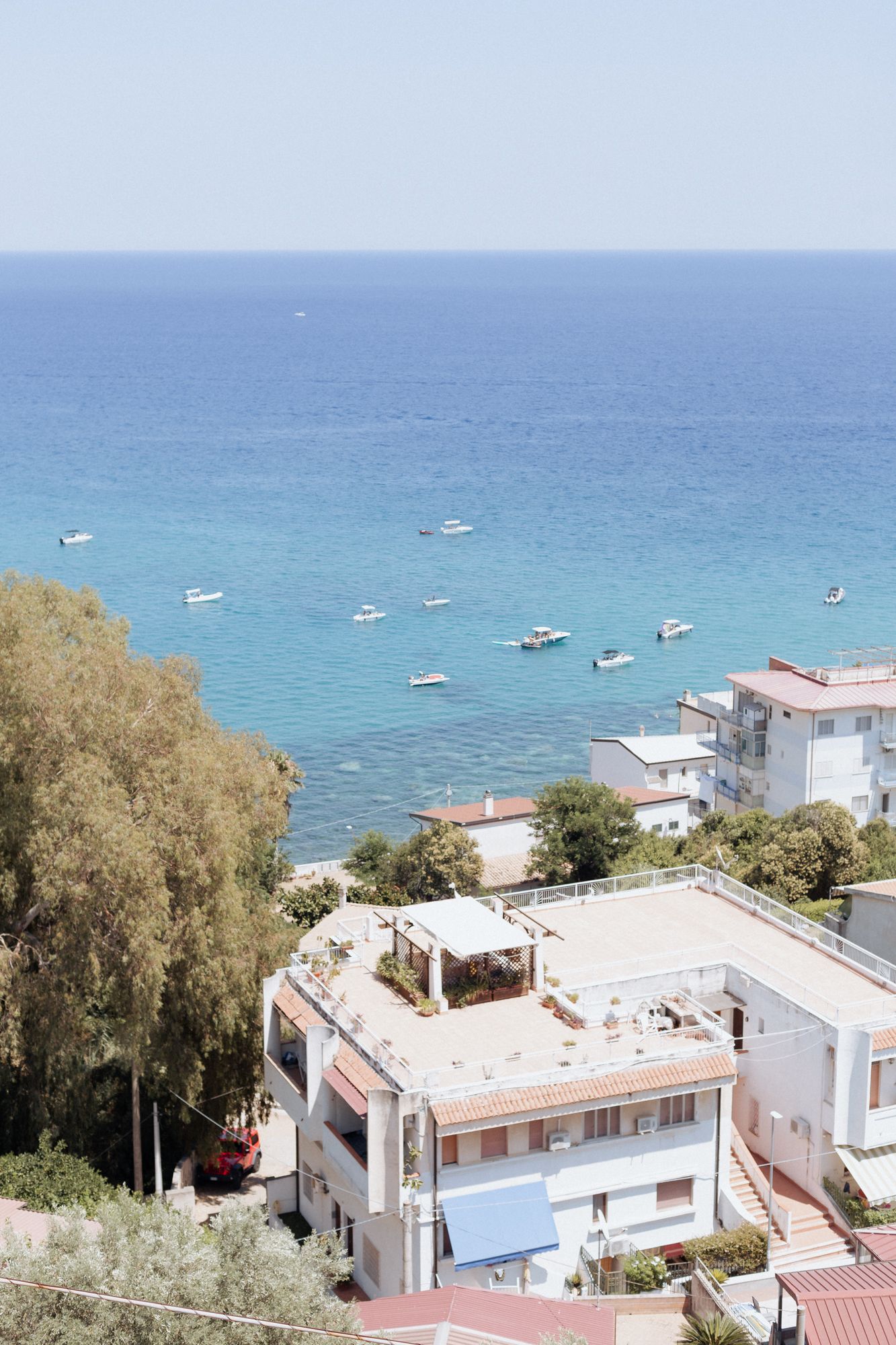 Aerial view of white coastal buildings with boats anchored in turquoise Mediterranean waters.