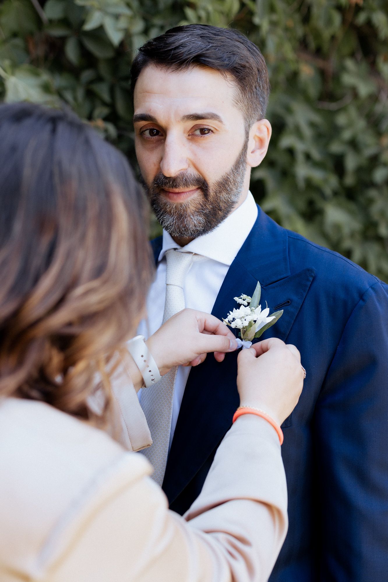 A boutonniere is pinned onto a navy blue suit jacket during a wedding ceremony.