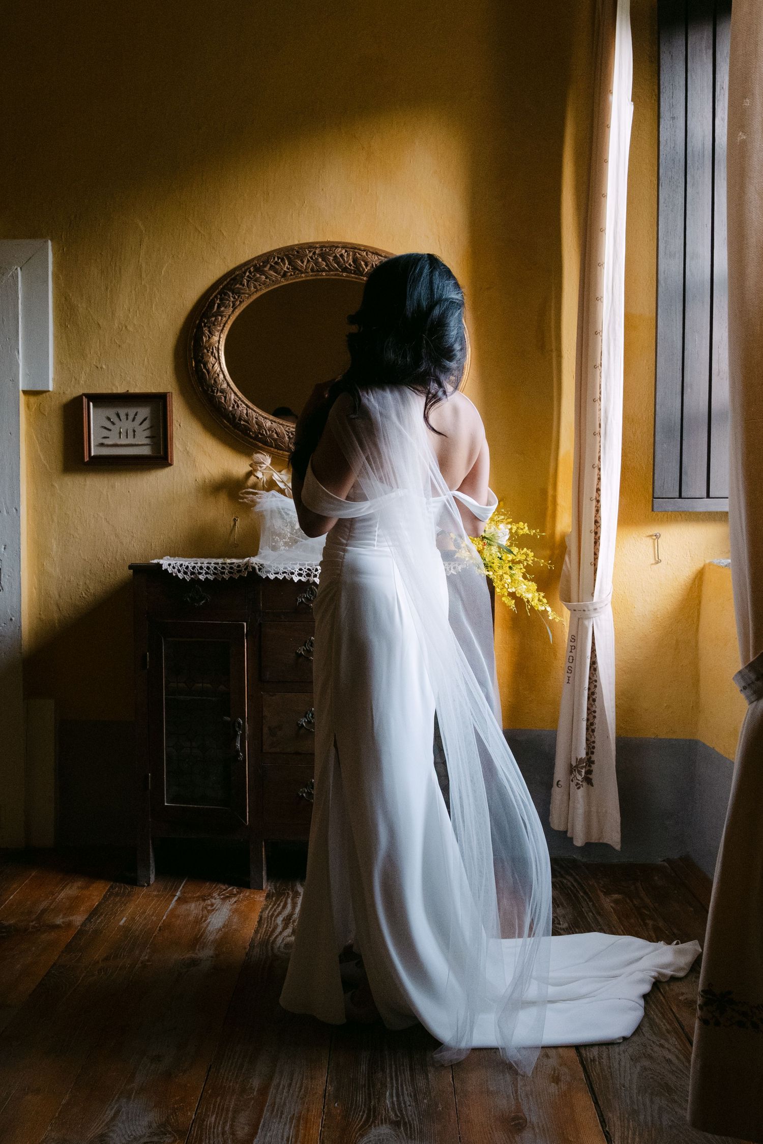 A white wedding dress displayed in a rustic room with wooden floors and warm lighting creates a romantic atmosphere.