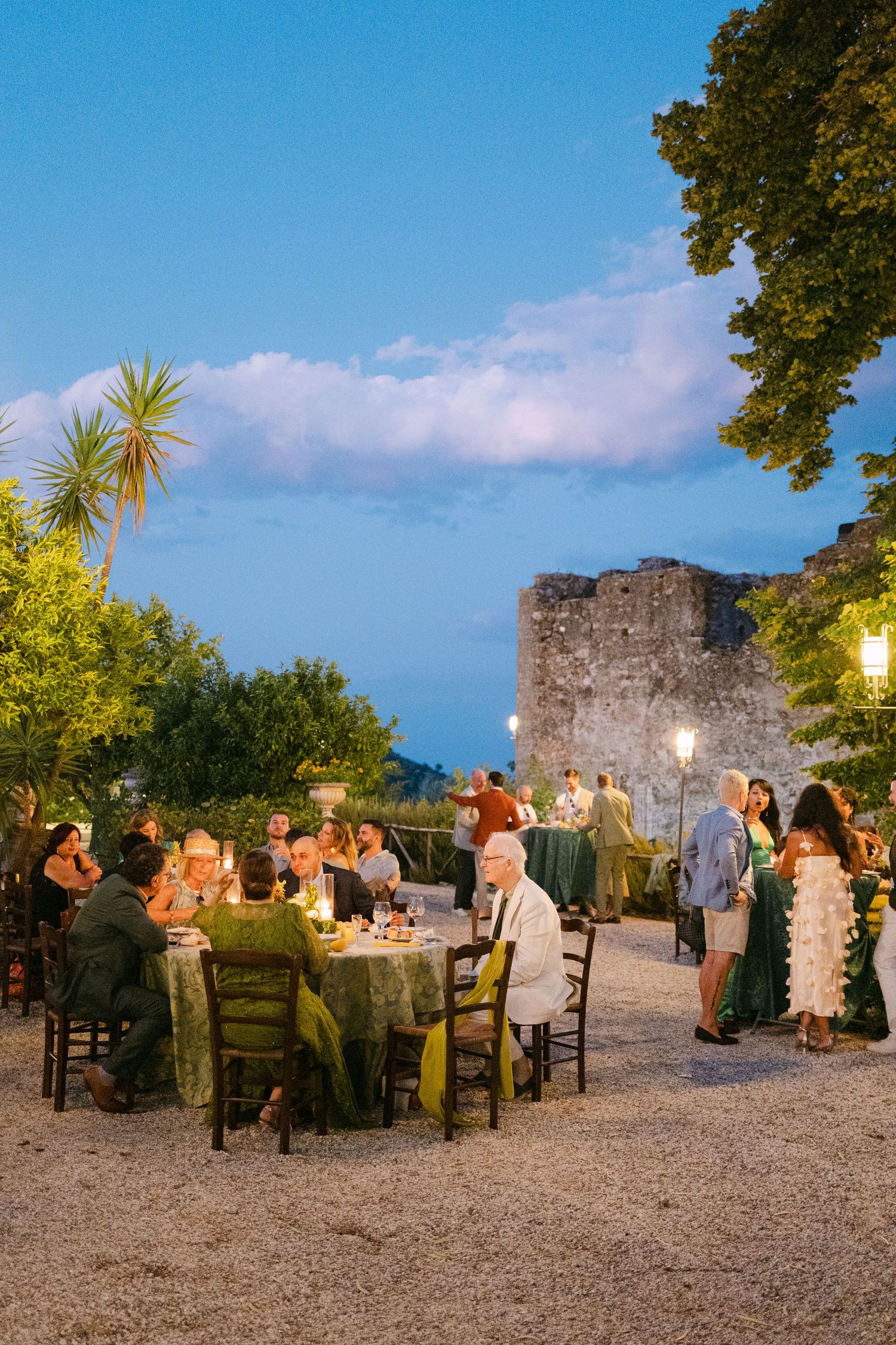 Wedding reception dinner tables set up outdoors at dusk near ancient stone ruins.