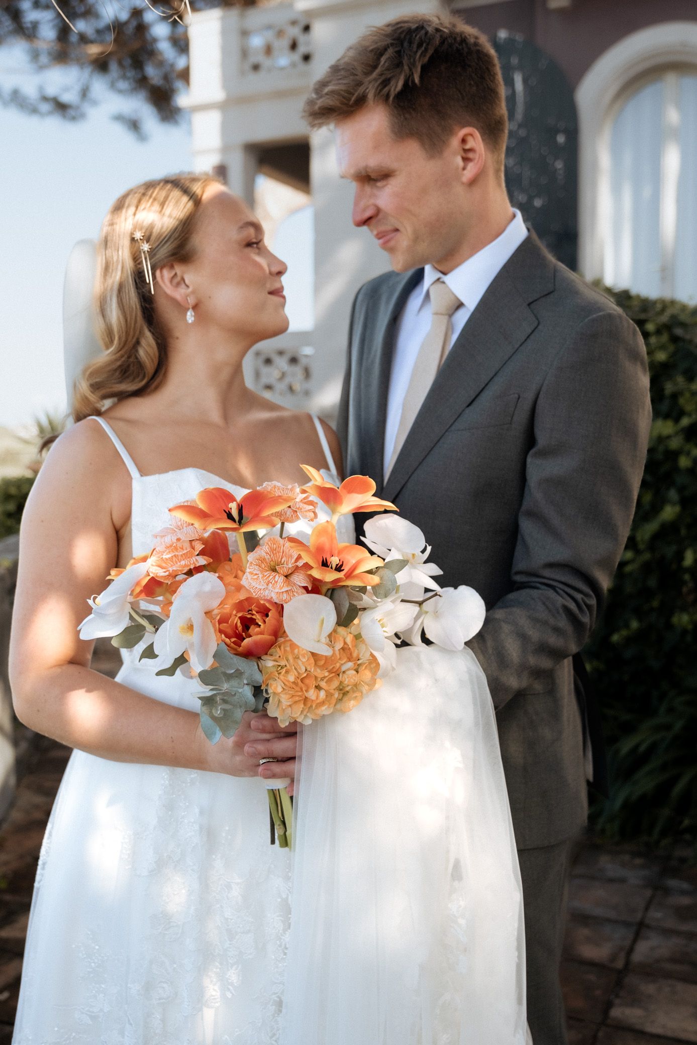 A romantic wedding moment outdoors with coral and white floral bouquets against a classic architectural backdrop.