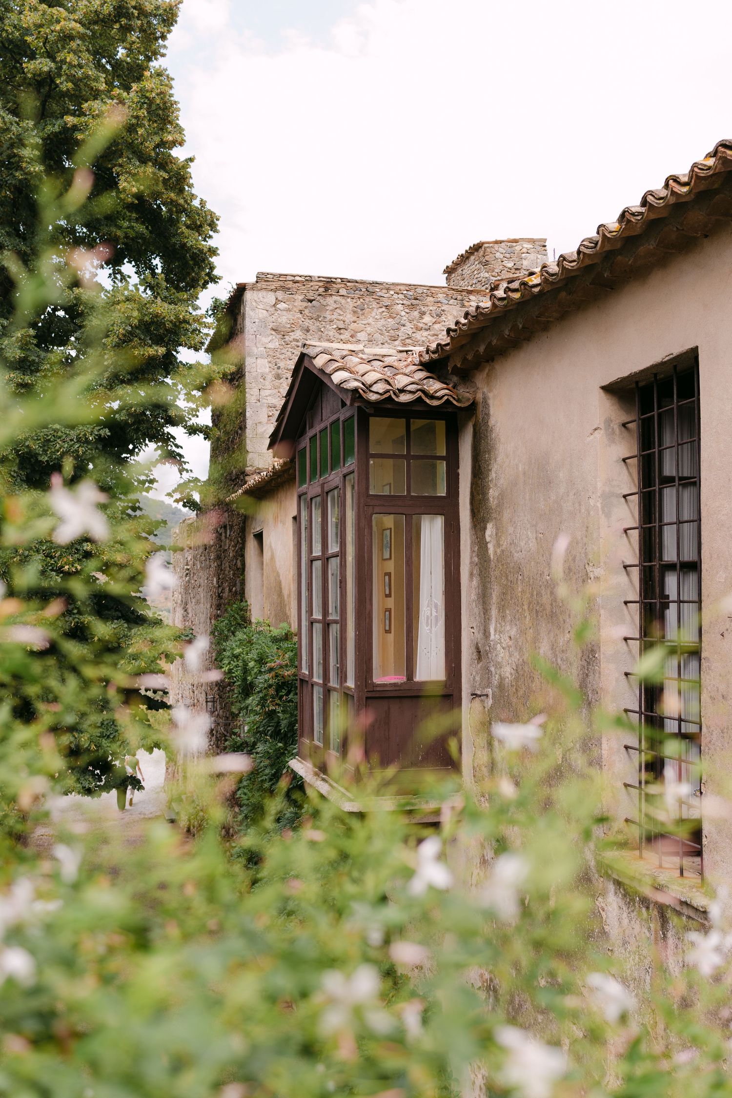 A series of vintage windows on an old stucco building with clay tile roof and lush greenery framing the view.
