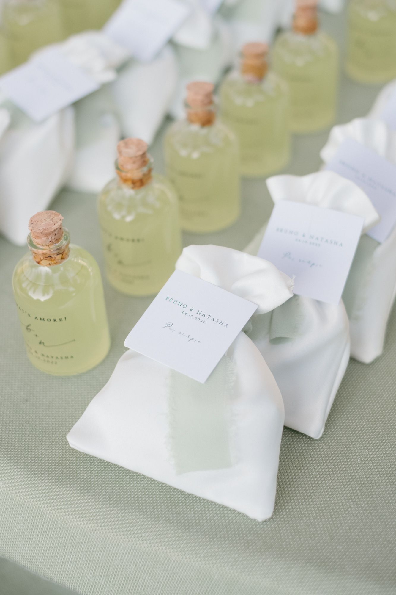 Small glass bottles with cork stoppers and white tags arranged in rows on a light gray textured surface.