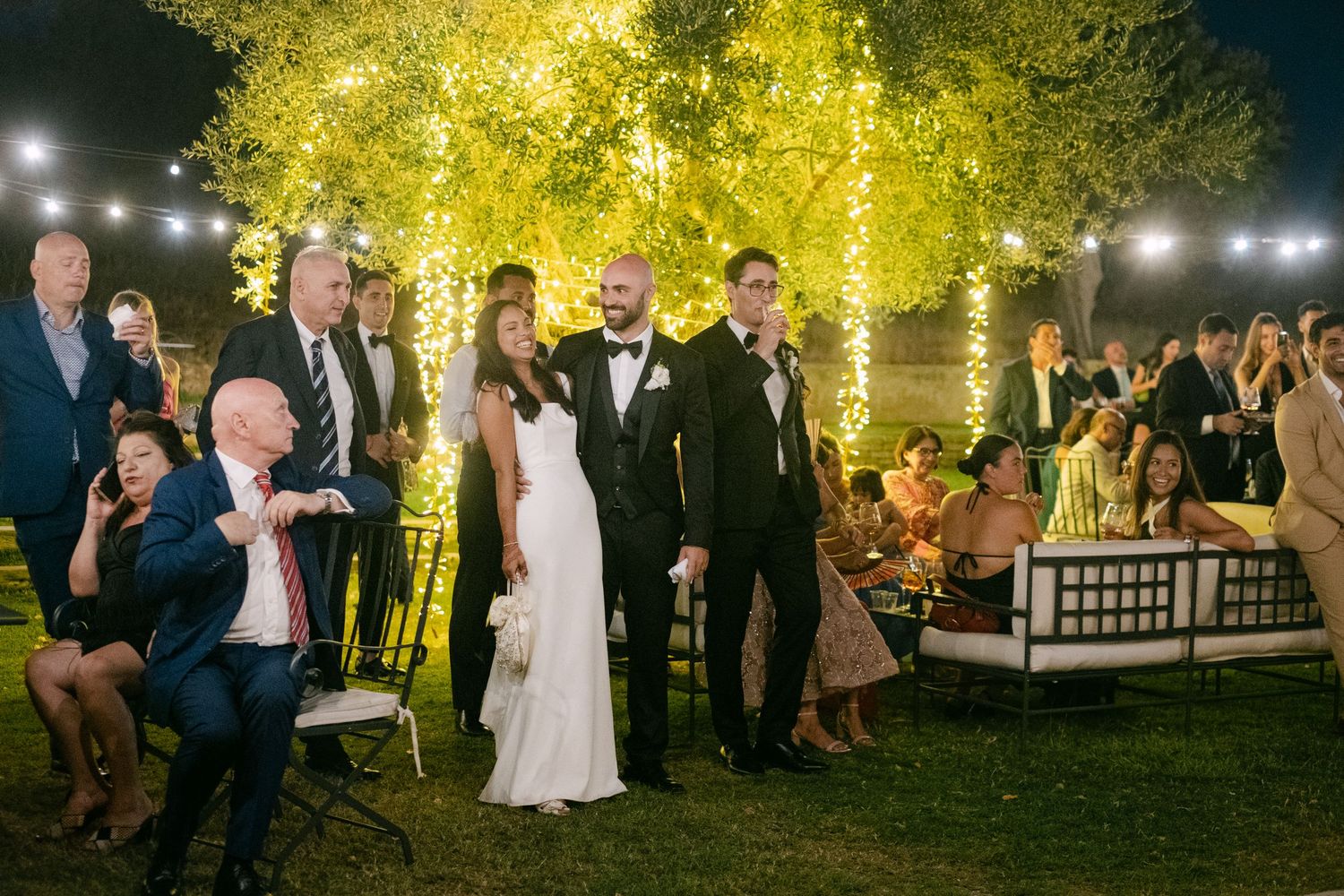 Wedding reception party at night with string lights illuminating guests and trees.