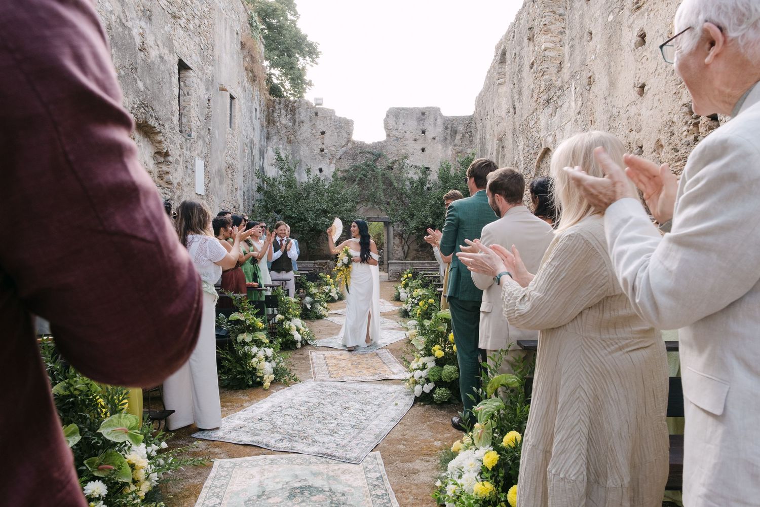 A couple in wedding attire embraces and shares a romantic moment in a rustic stone alleyway with greenery.