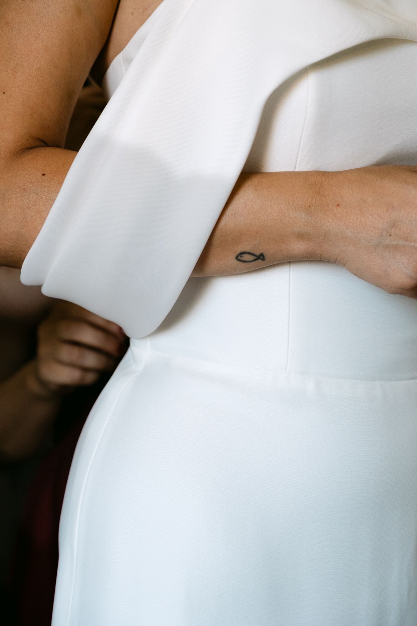 Close-up detail of white fabric draping against skin with a small tattoo visible.