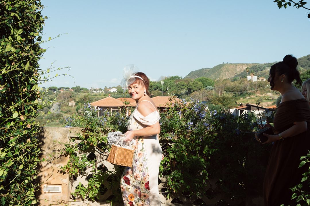 Wedding guests gather outdoors on a sunny day surrounded by natural greenery.