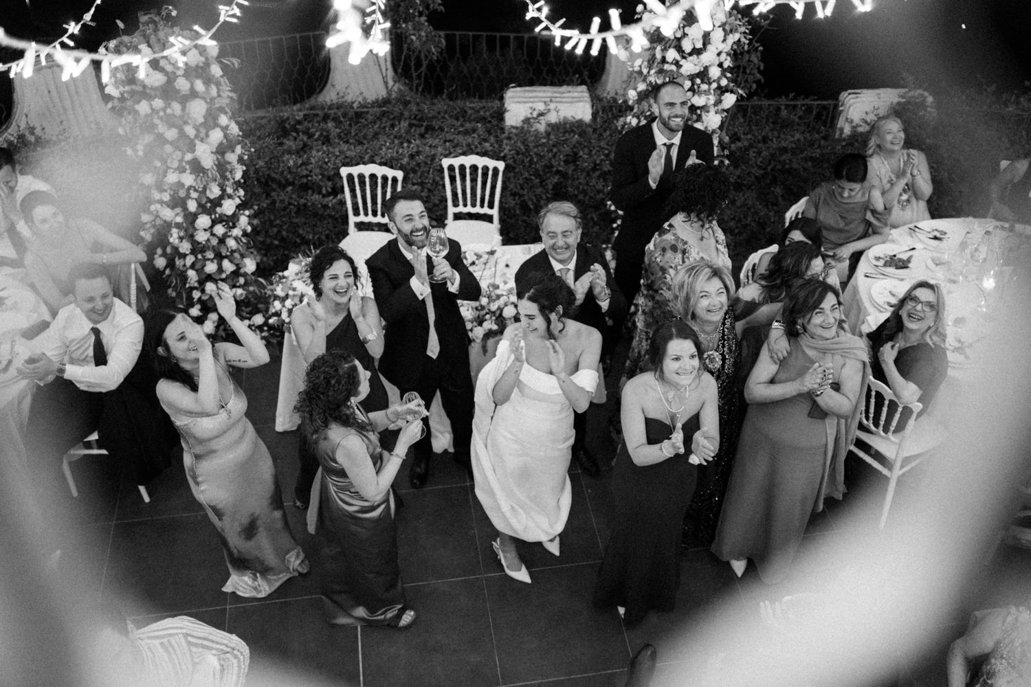 Black and white photo of wedding guests dancing and celebrating on a crowded dance floor.